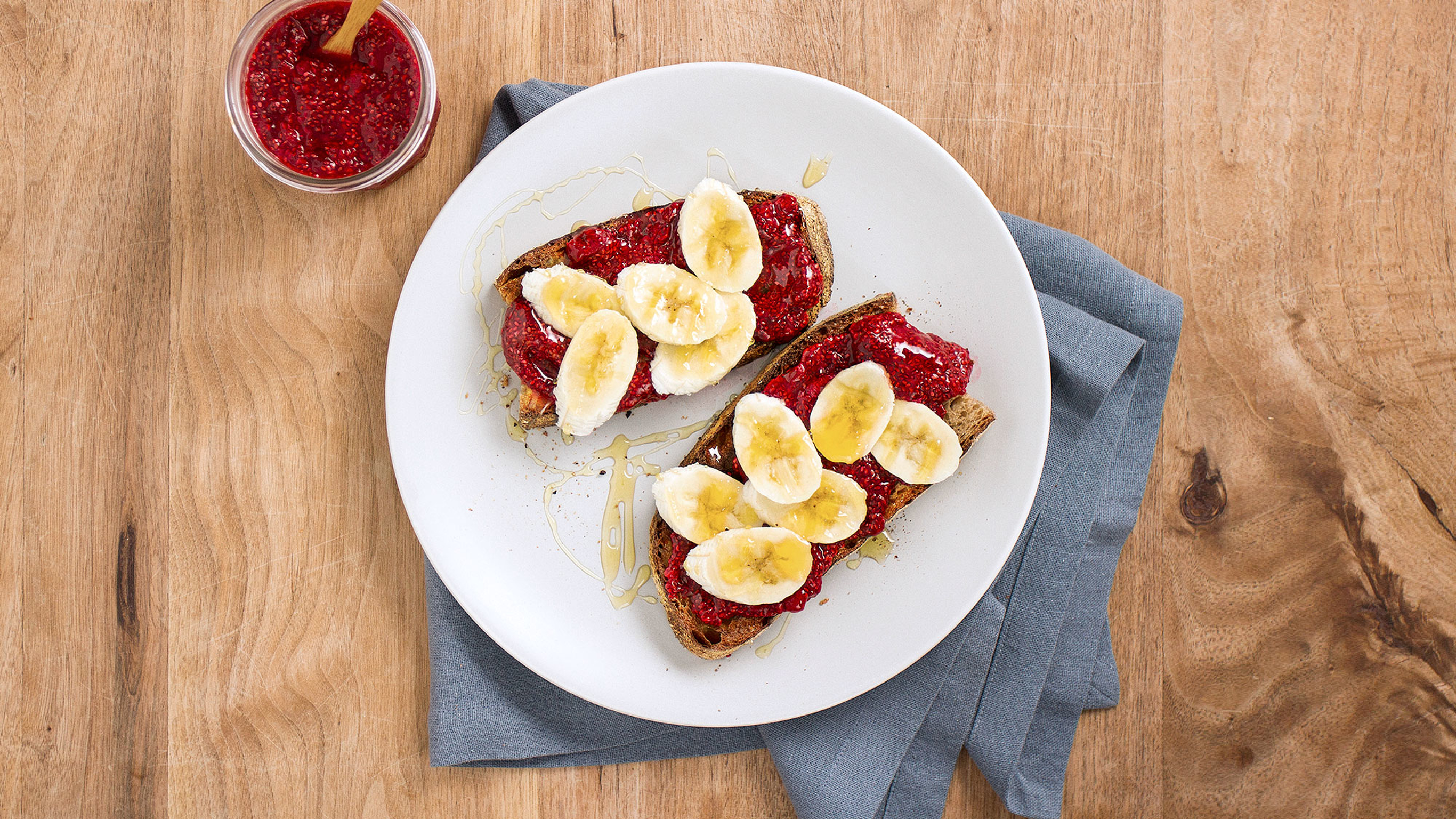 A plate of Easy Chia Jam on Toast sits on a wooden table, with a grey linen napkin on the side.