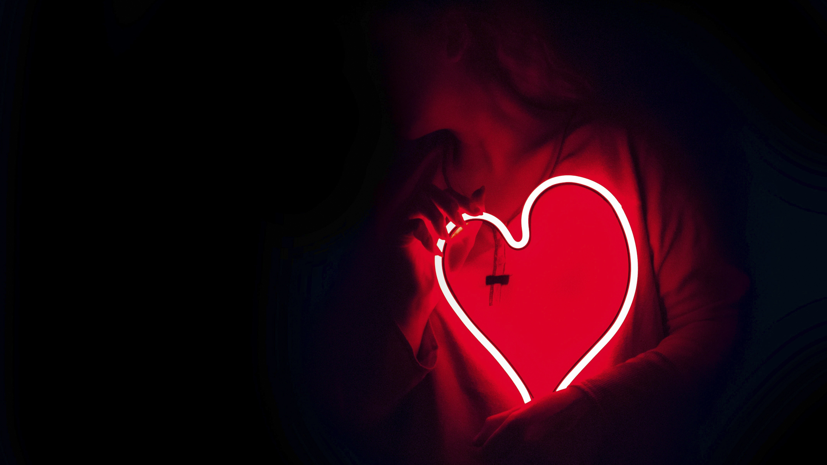 A person in the dark holds a neon red love heart.