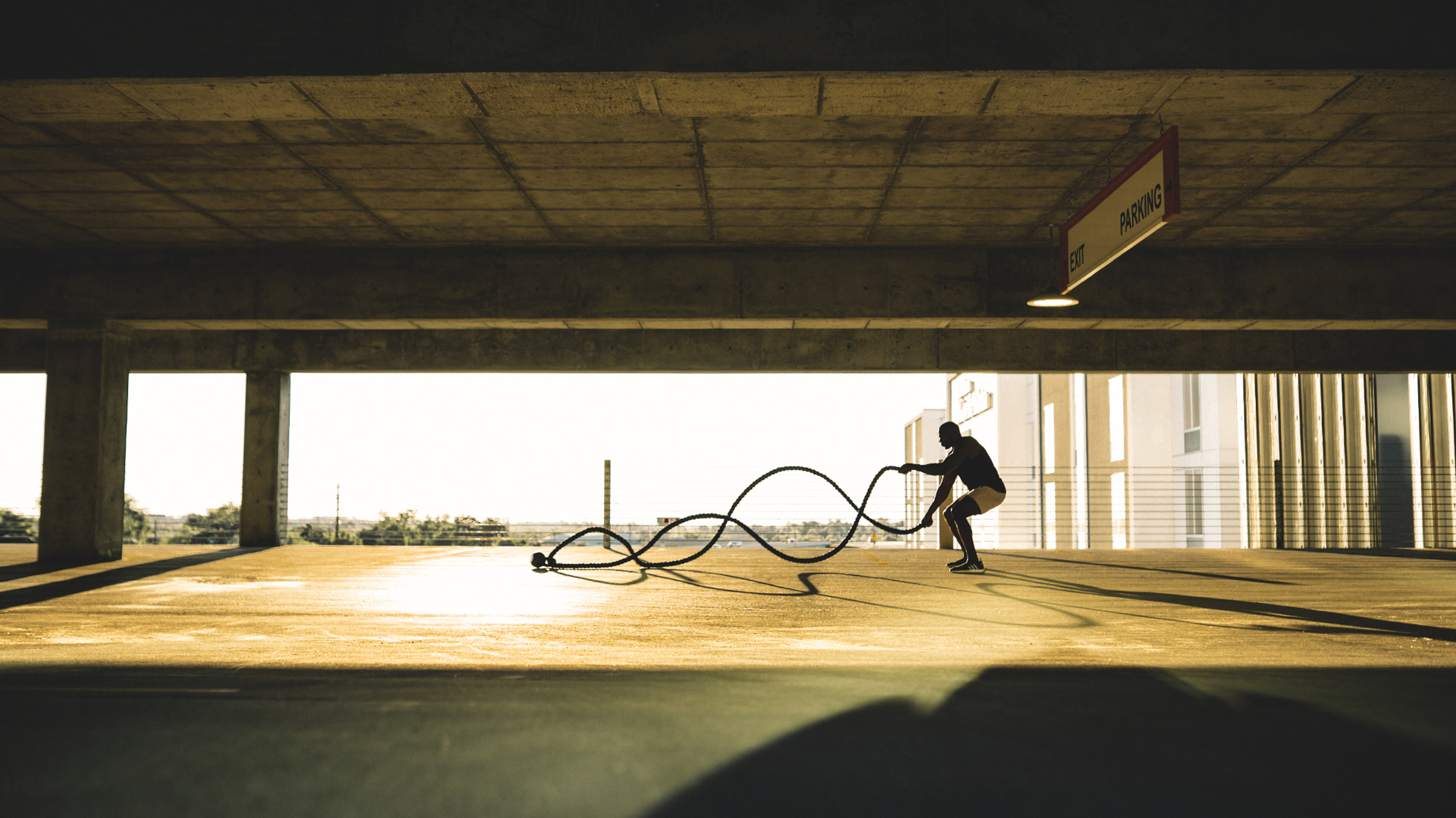 A man works out with Battle Ropes in a multi-level car park.