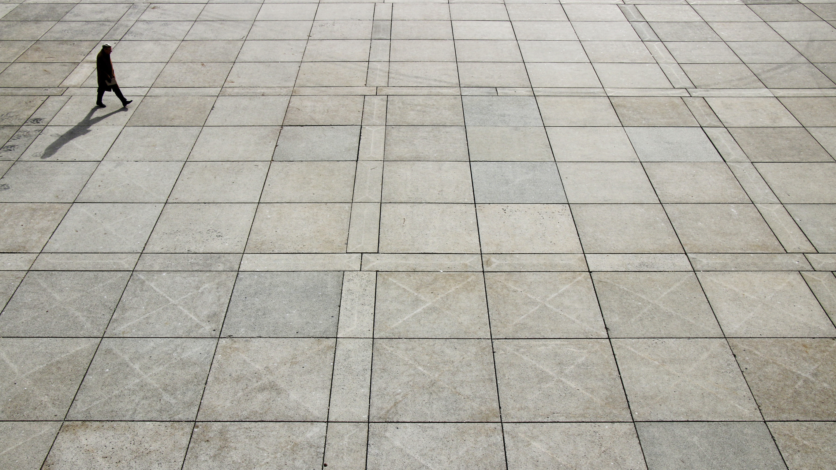 A birds eye view of a man in a dark coat walking across a square.