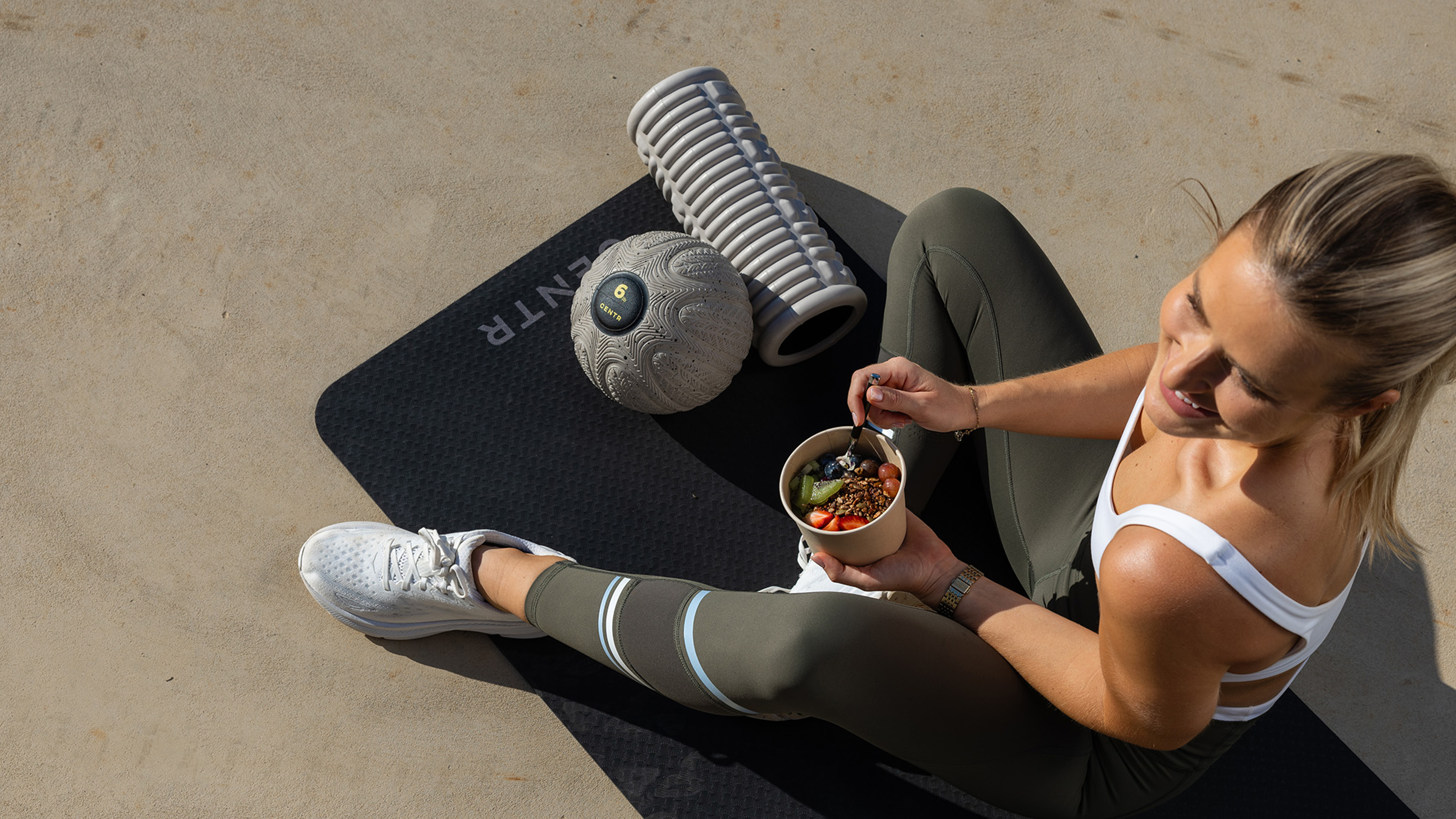 Centr trainer Alexz Parvi sits on a workout mat and enjoys a healthy, nutritious snack from the Centr recipe library.