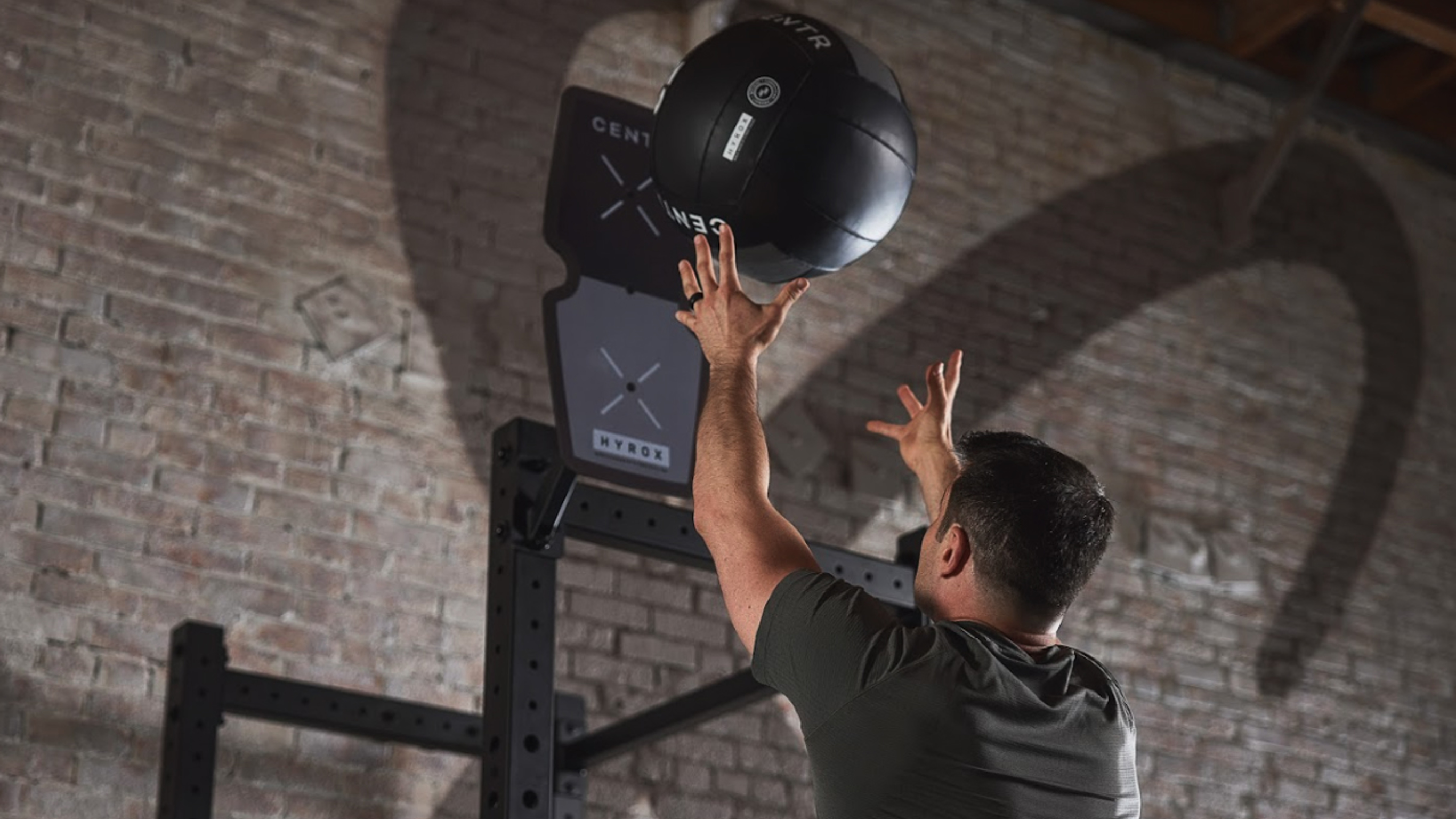 A man throws a Centr x Hyrox branded wall ball at a target.