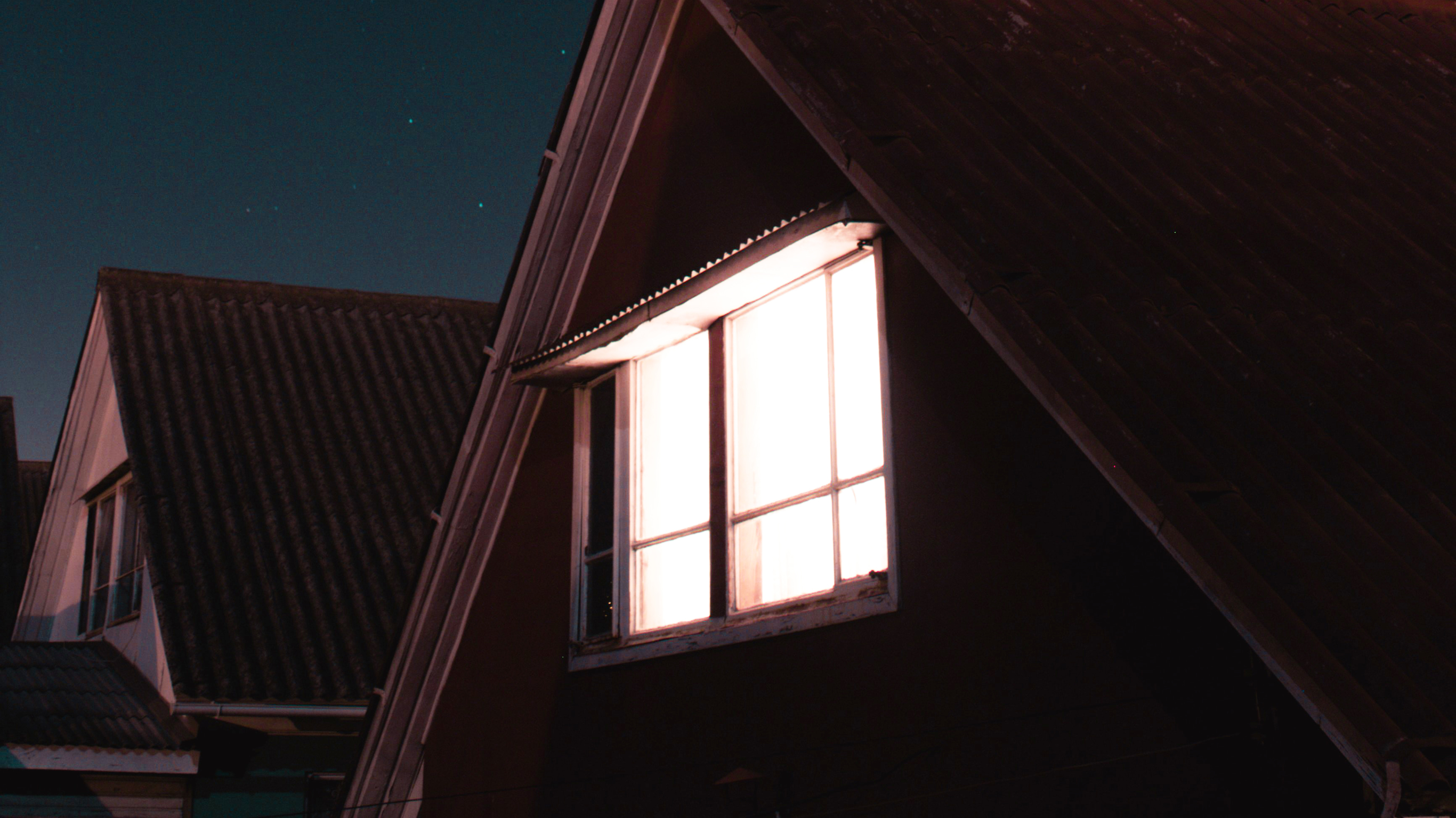 A night-time light shines through a curtained window on the second floor of a suburban house