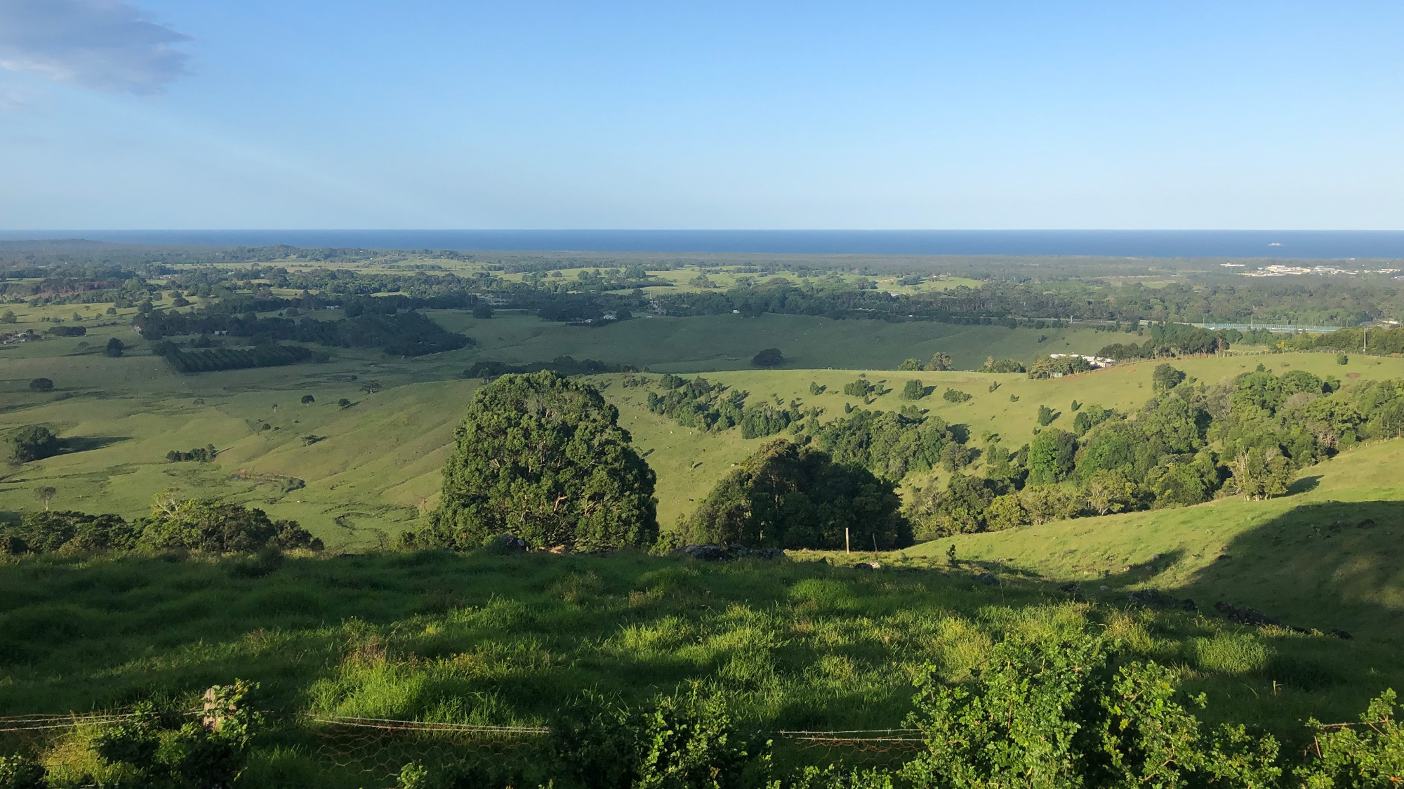 A green vista with rolling hills and in the ocean in the background.