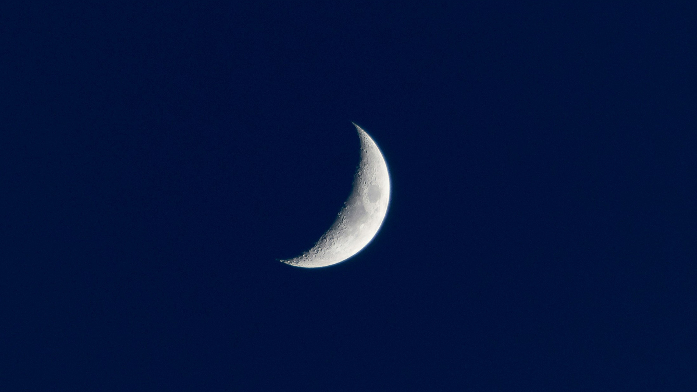 A close-up photograph of a crescent moon against a dark blue night sky.