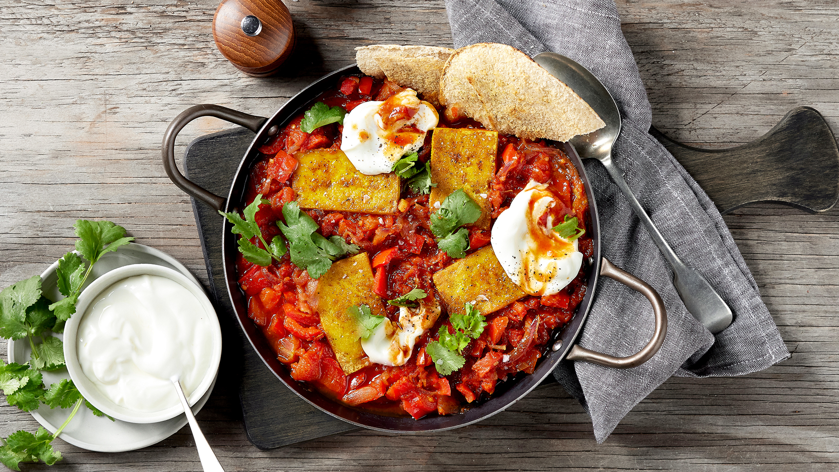 A pan of Centr's Tofu Shakshuka rests on a wooden board on a grey table, ready for serving.