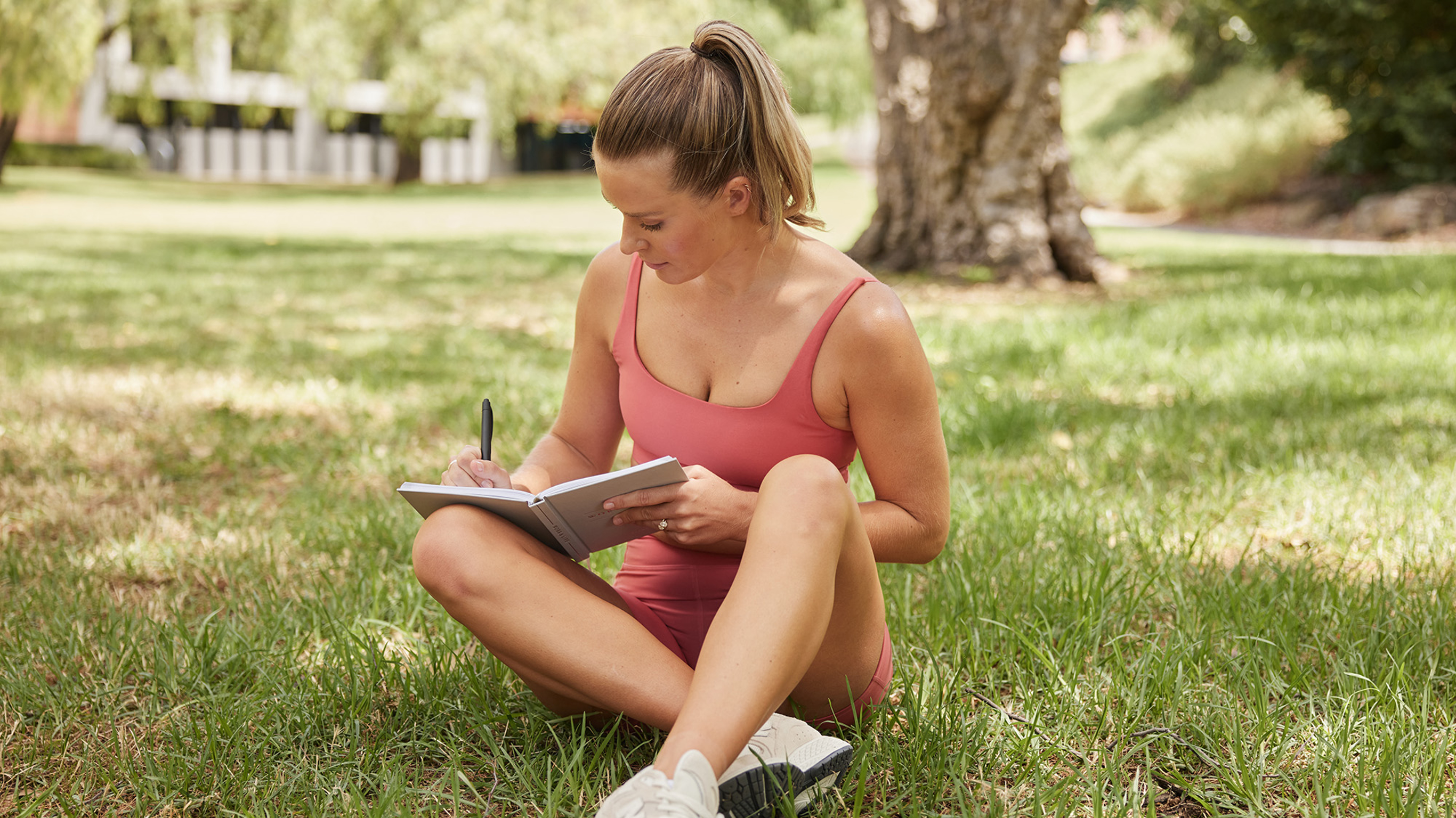Centr trainer Alexz Parvi sits in a grassy park and writes in a notebook.