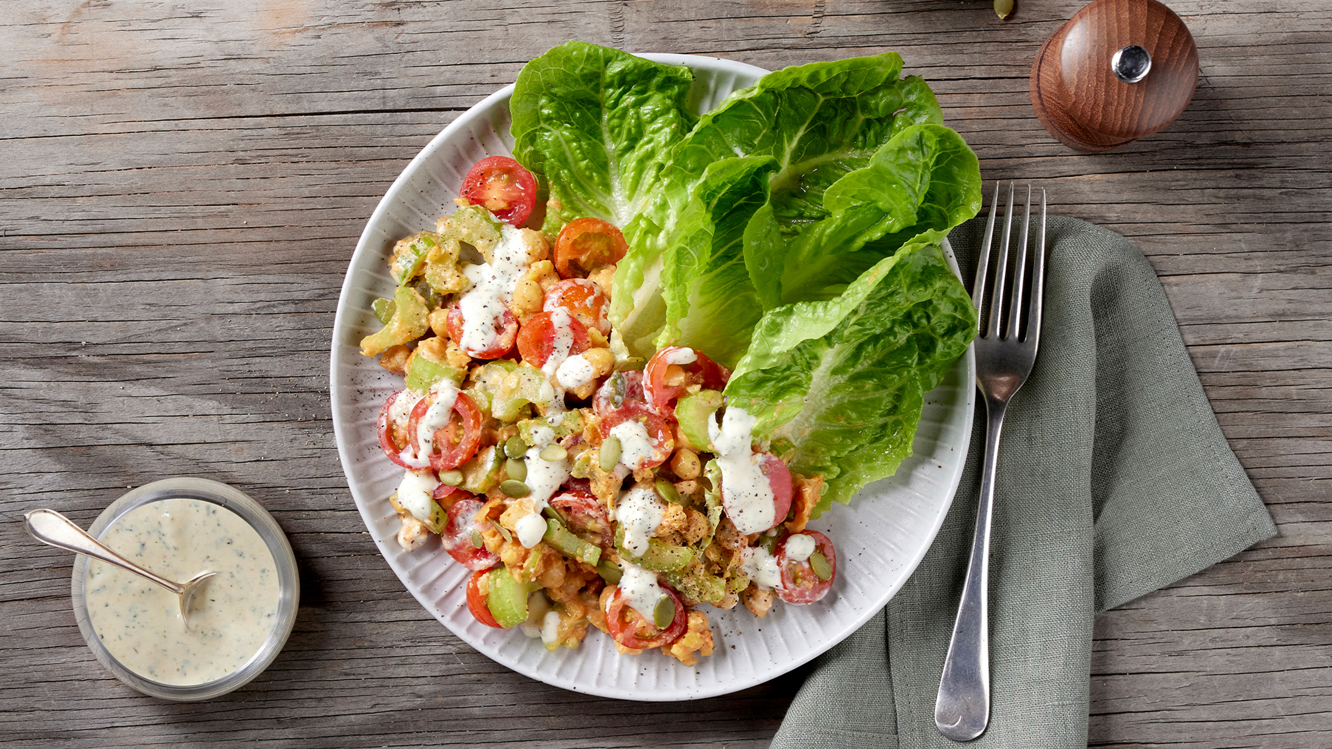 Buffalo chickpea salad on a table with dressing and cutlery.