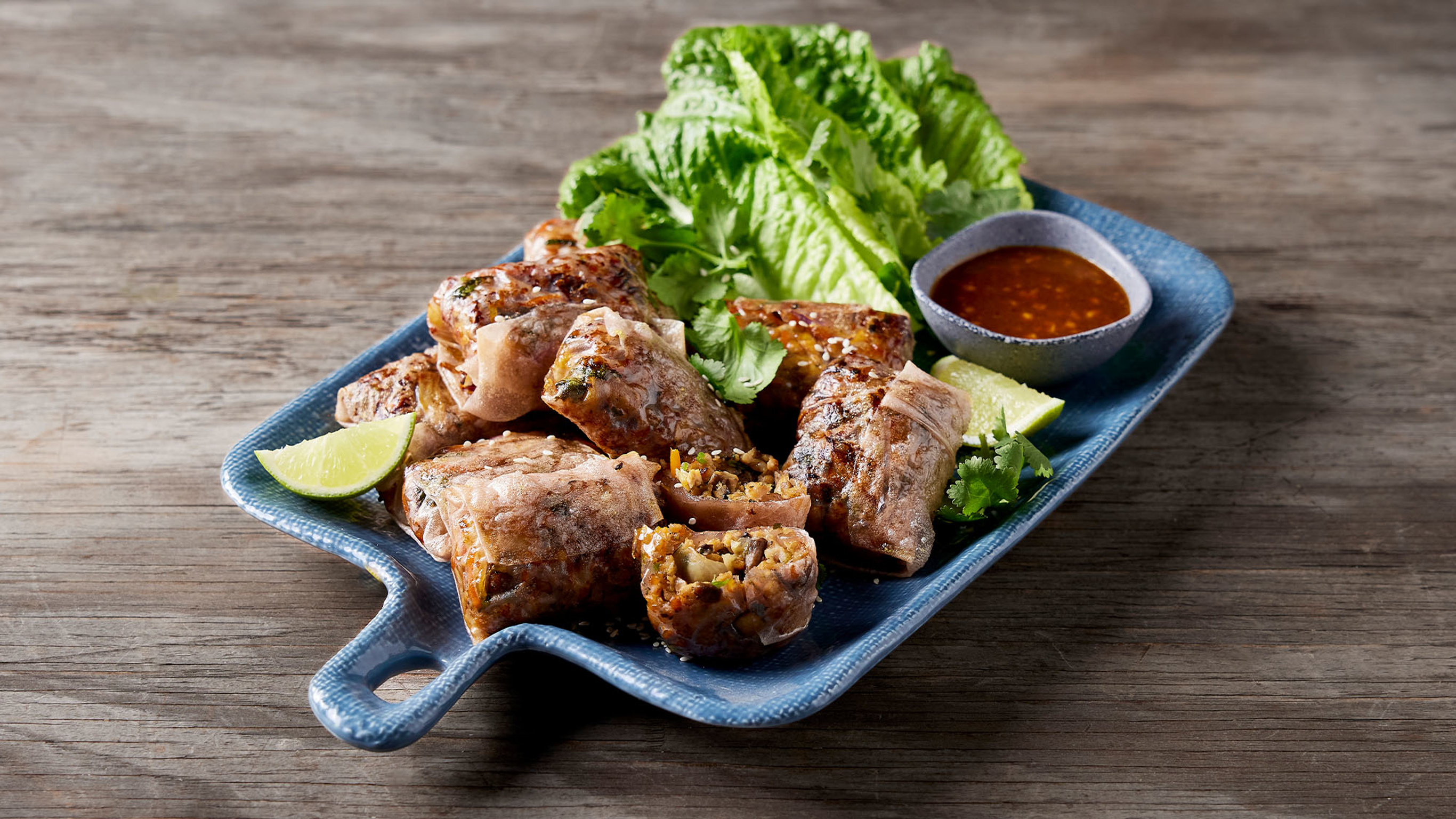 Centr's air fryer chicken and mushroom parcels are piled up on a rectangular, blue serving dish, with lettuce leaves and dipping sauce.