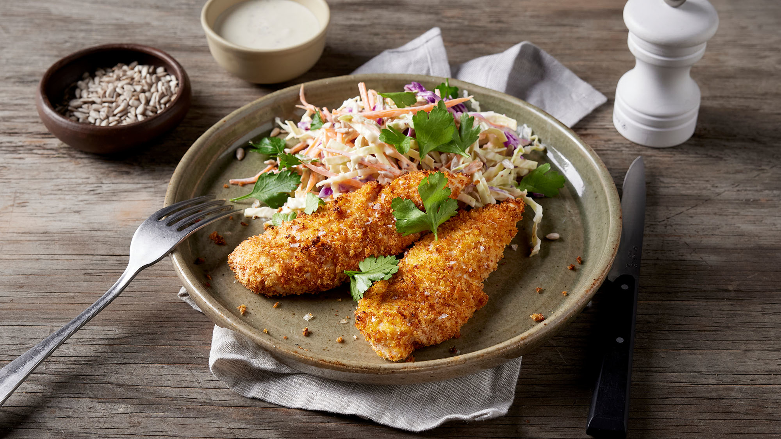 A serve of Centr's air fryer chicken tenders and slaw sits on a round, rimmed earthern-ware dinner plate, ready for eating.