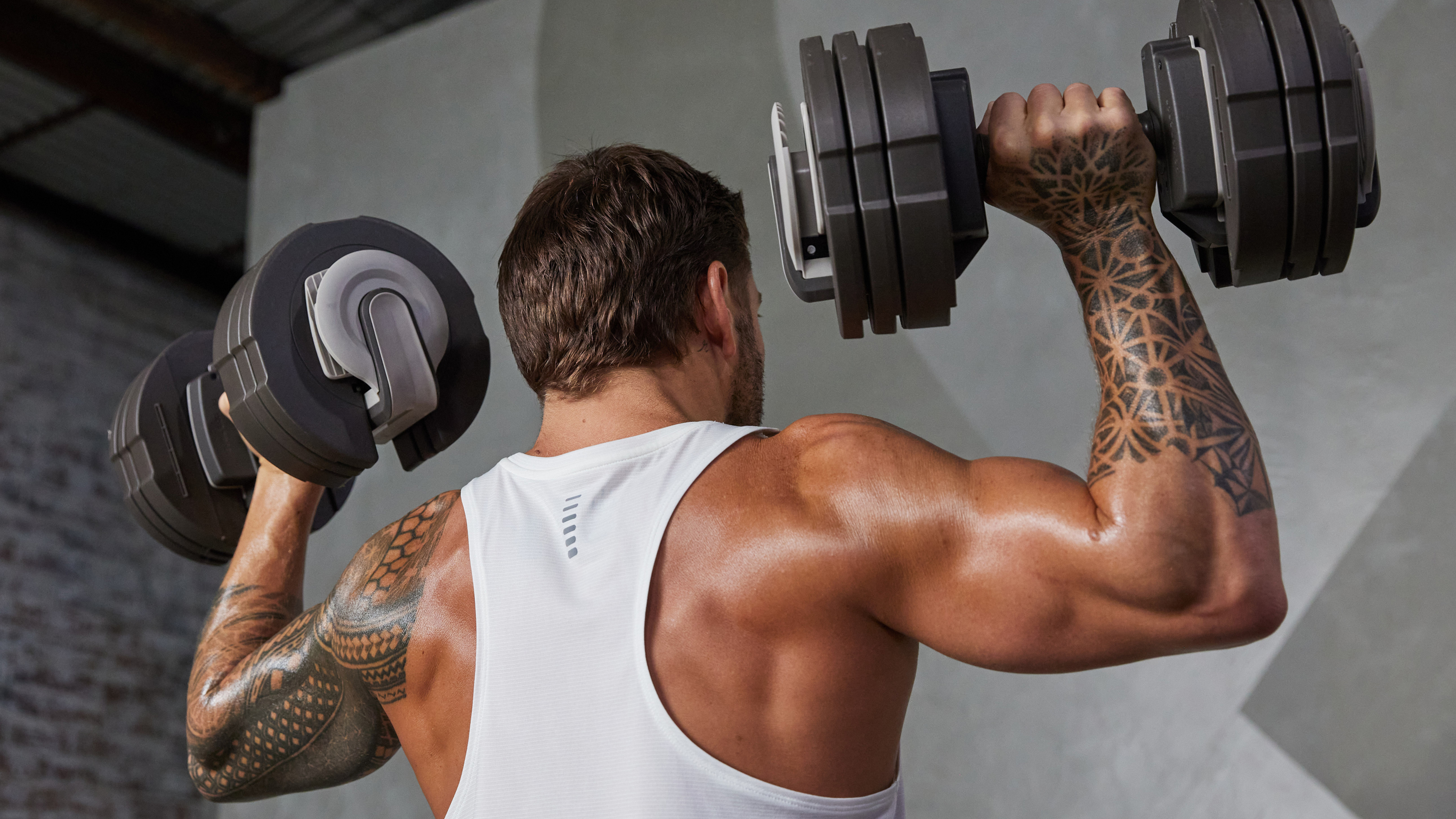 Centr trainer Luke Zocchi performs a shoulder press with a pair of adjustable dumbbells.
