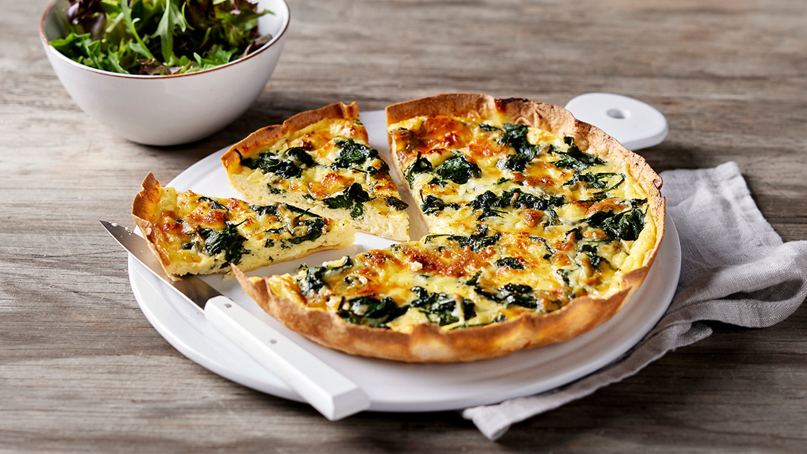 Sliced Spinach & Cheese Tortilla Quiche sits on a white ceramic serving platter, ready for serving.