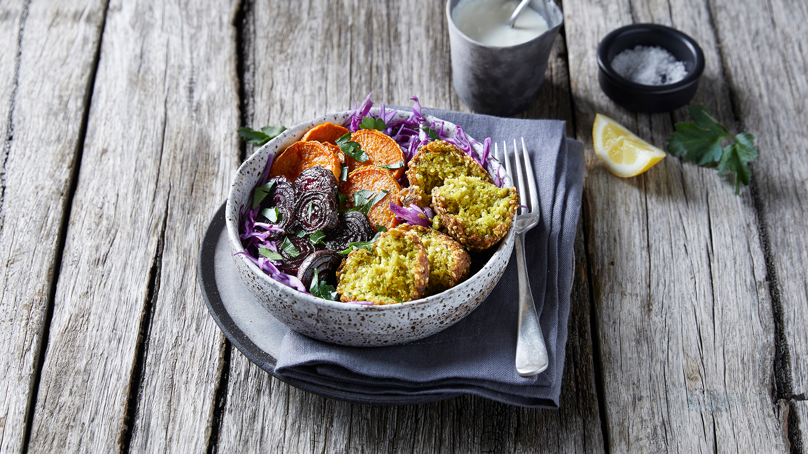 A bowl of Centr's Roast Vegetable Salad with Falafel sits on a lavendar-coloured napkin, ready to eat.