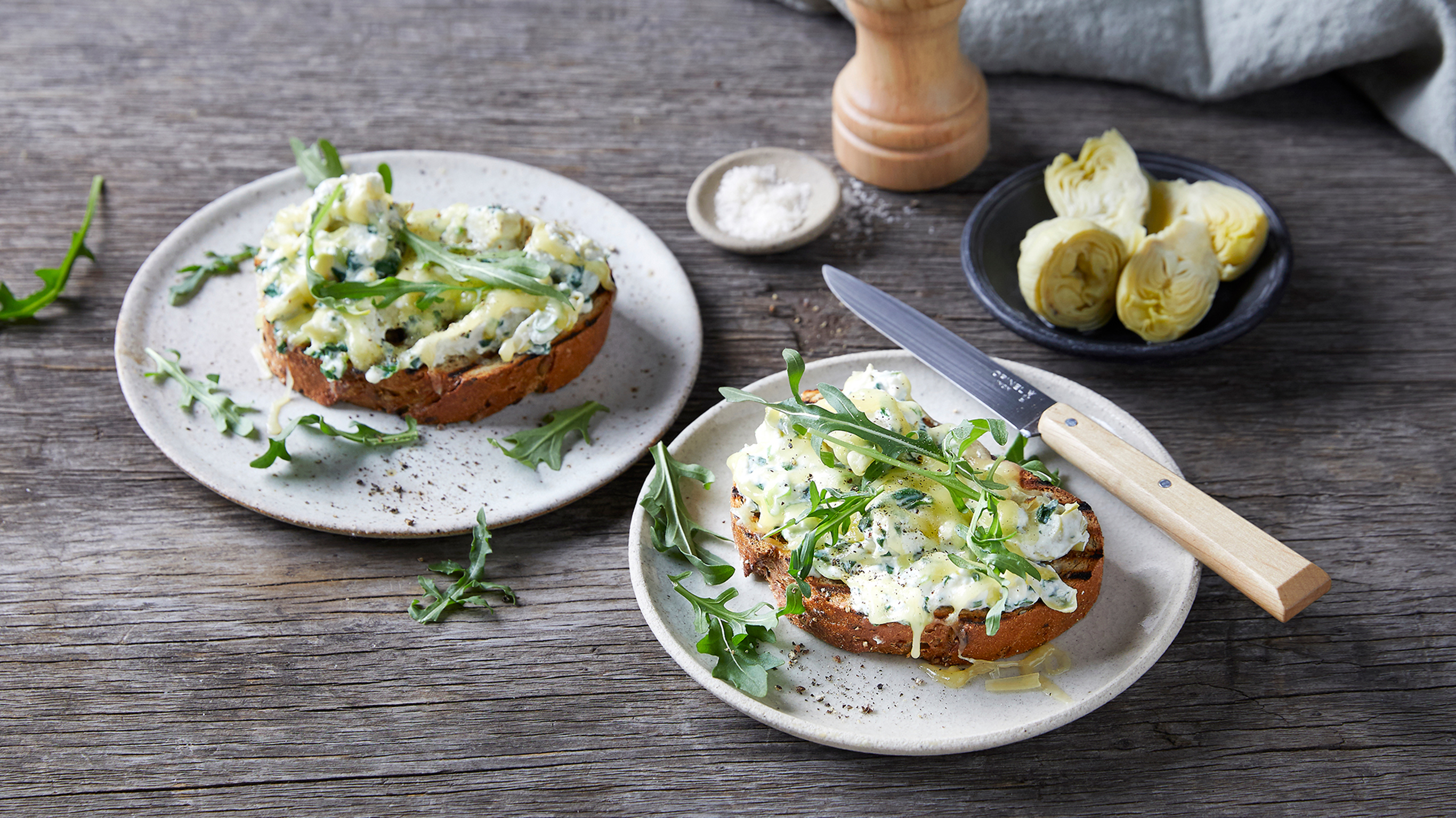 Two plates sit side by side with a serve of Spinach & Artichoke Bruschetta on each.