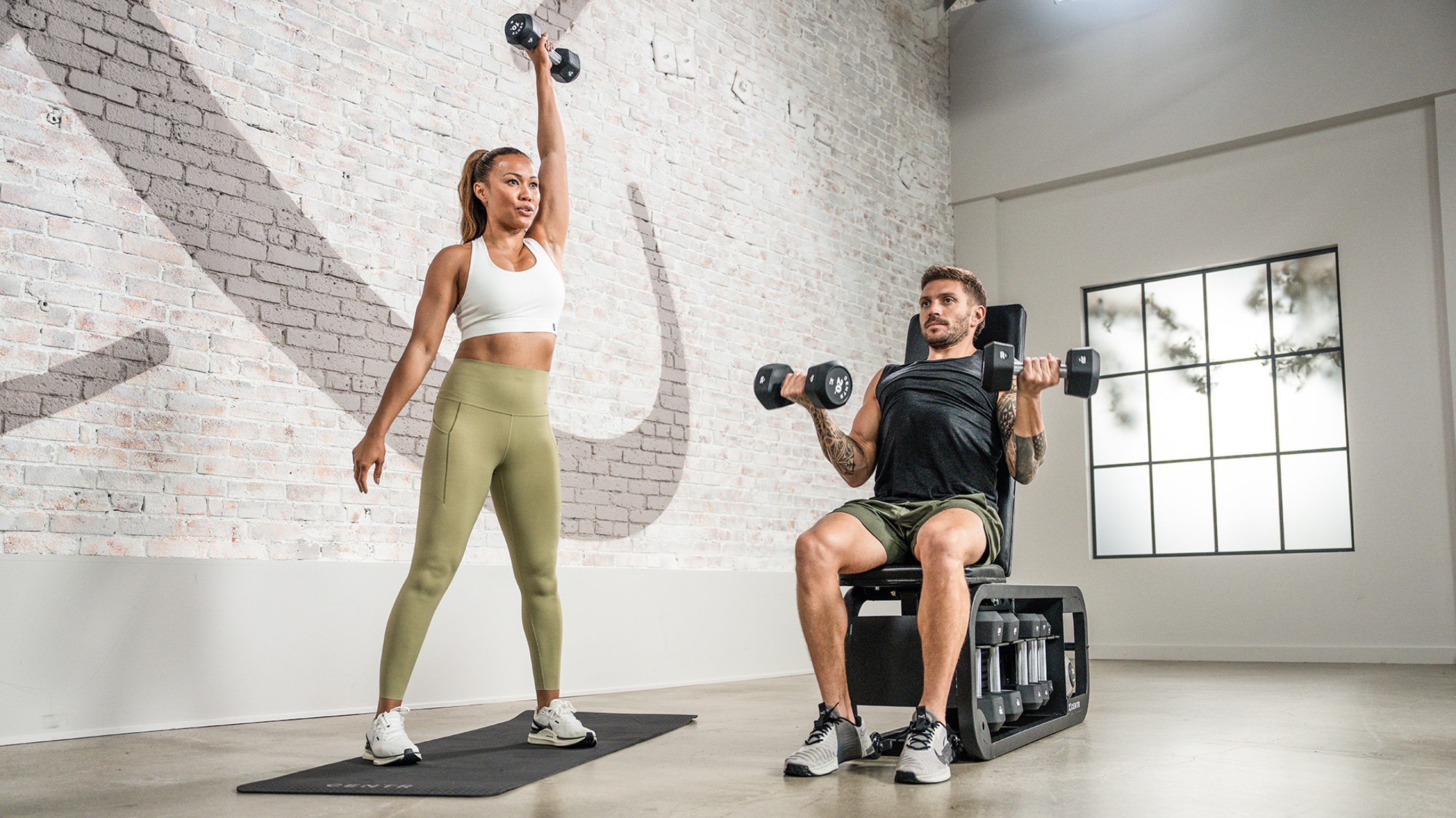 Centr trainers Maricris, Luke and Dan pose holding dumbbells around a bench.