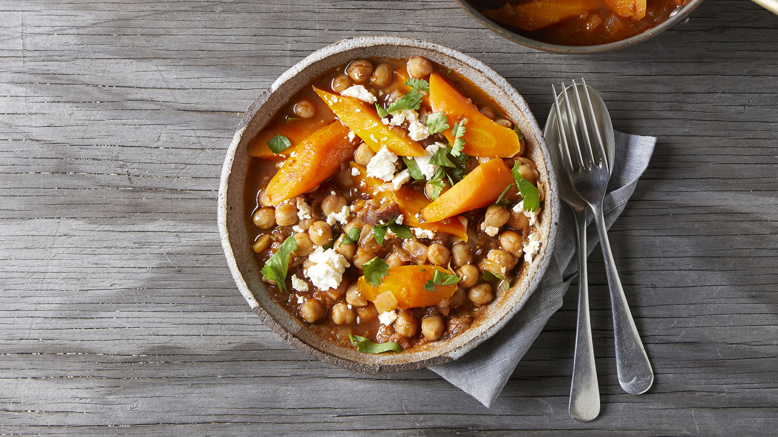 A serve of Centr's Chickpea Braise with Feta & Dates sits on a table ready to eat.