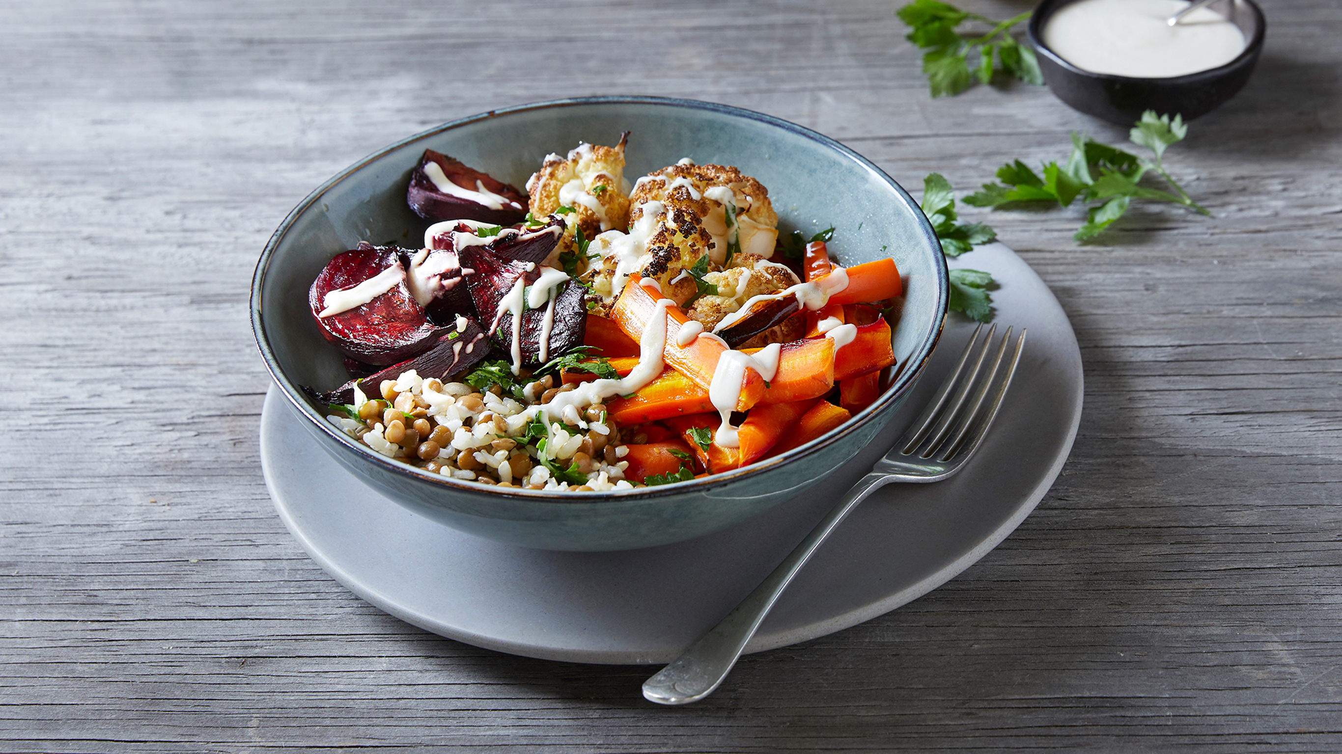 A bowl of Roasted Vegetable Rice Bowls with Tahini Dressing from the Centr menu sits on a woden table ready for eating.