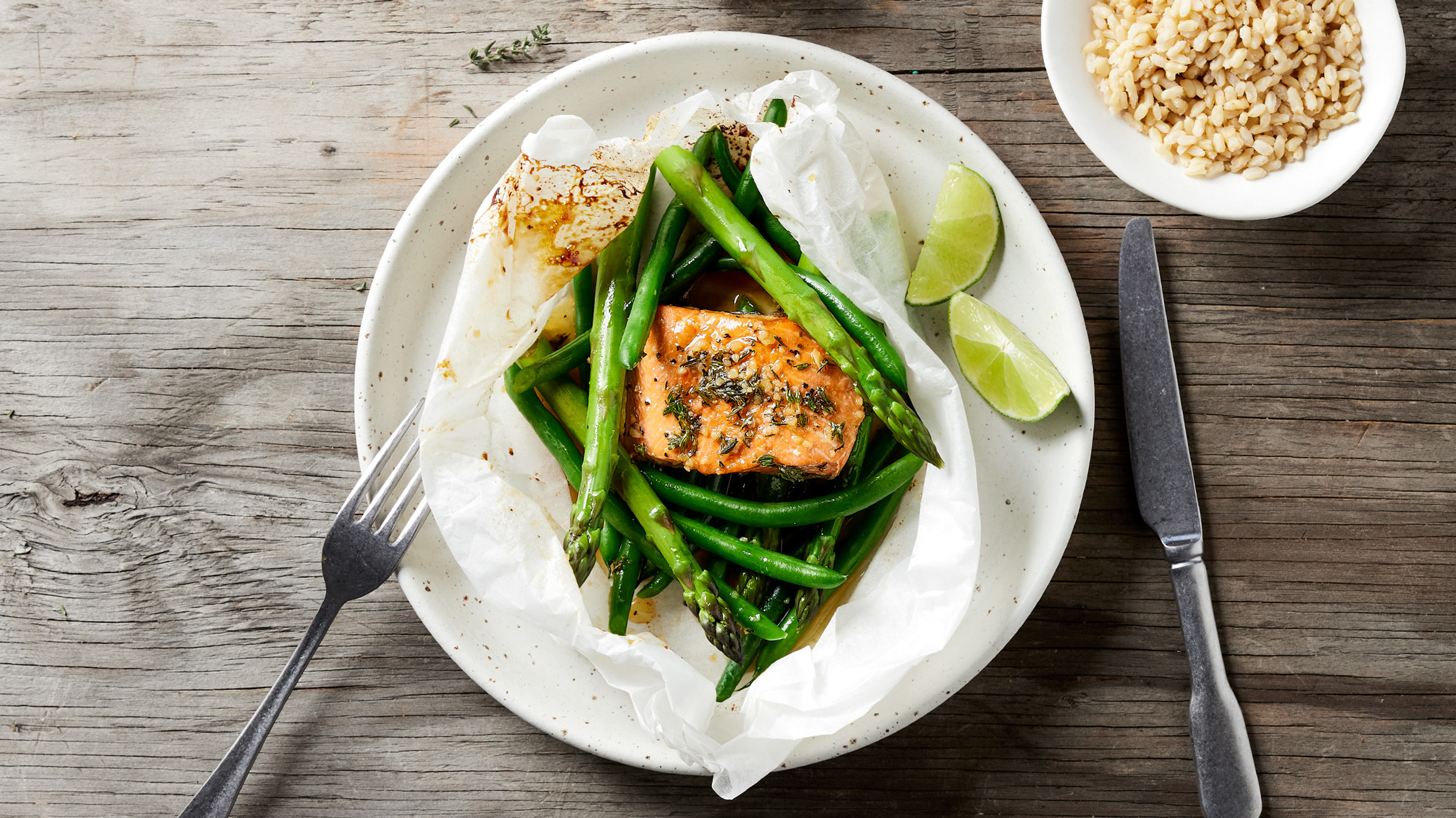 A plate of Centr's Simple Baked Salmon with Honey Lemon Sauce sits on a wooden table with knife and fork ready for eating.