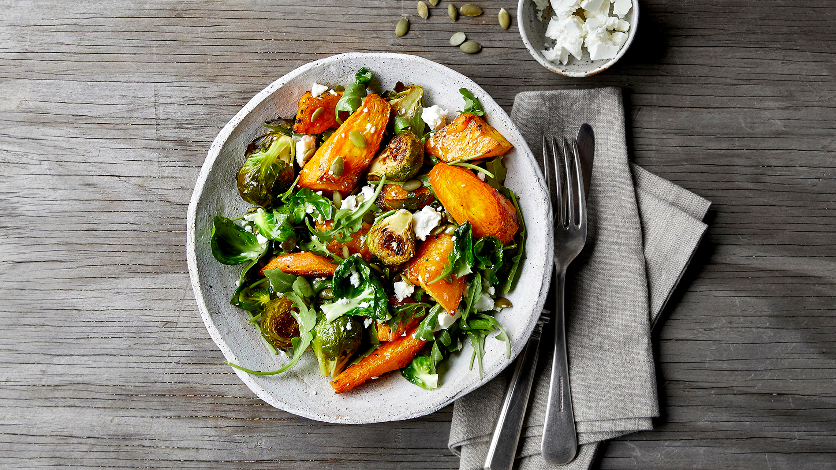 A overhead view of a plate of Centr's Roast Vegetable Salad, with a grey linen napkin and silver knife and fork on the side.