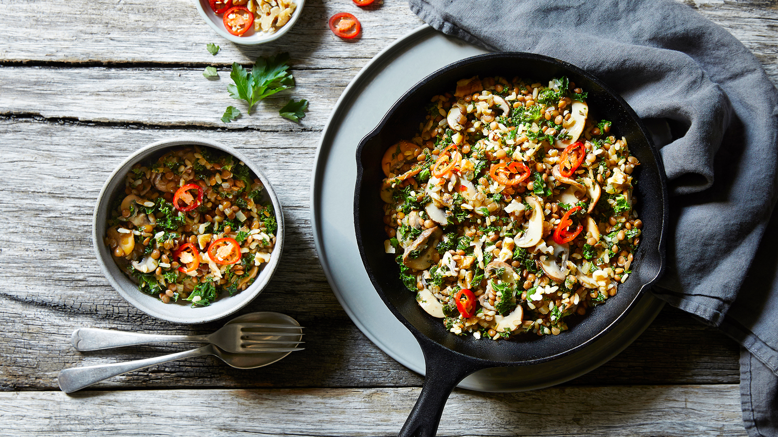 A bowl of Centr's Lentil Fried Rice with Kale & Mushrooms sits beside a skillet pan, ready for eating.