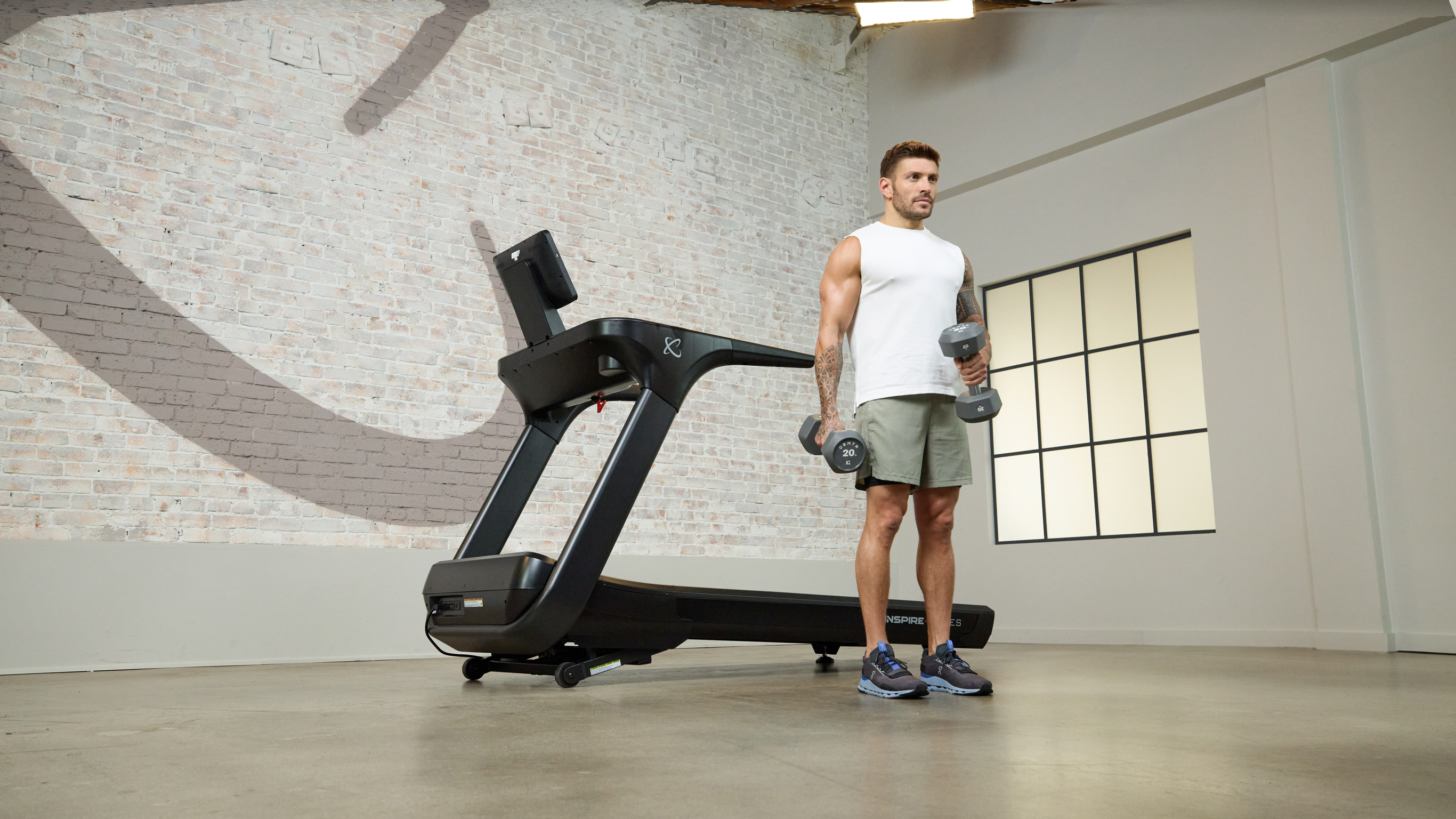 Centr trainer Luke Zocchi stretches beside a Centr treadmill in the Centr studio gym.