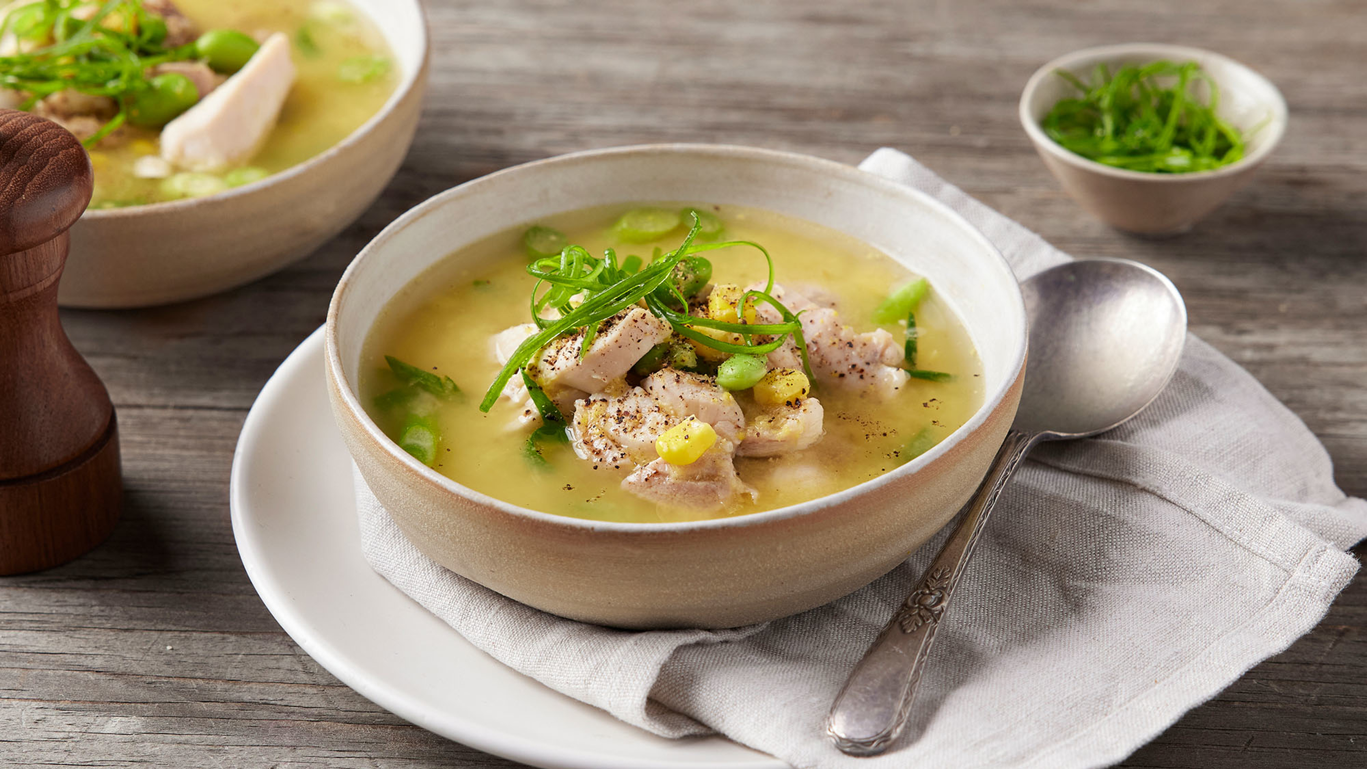 A bowl of Centr's Chicken and Corn soup sits on a napkin on a plate, wiith silver spoon on the side, ready for eating.