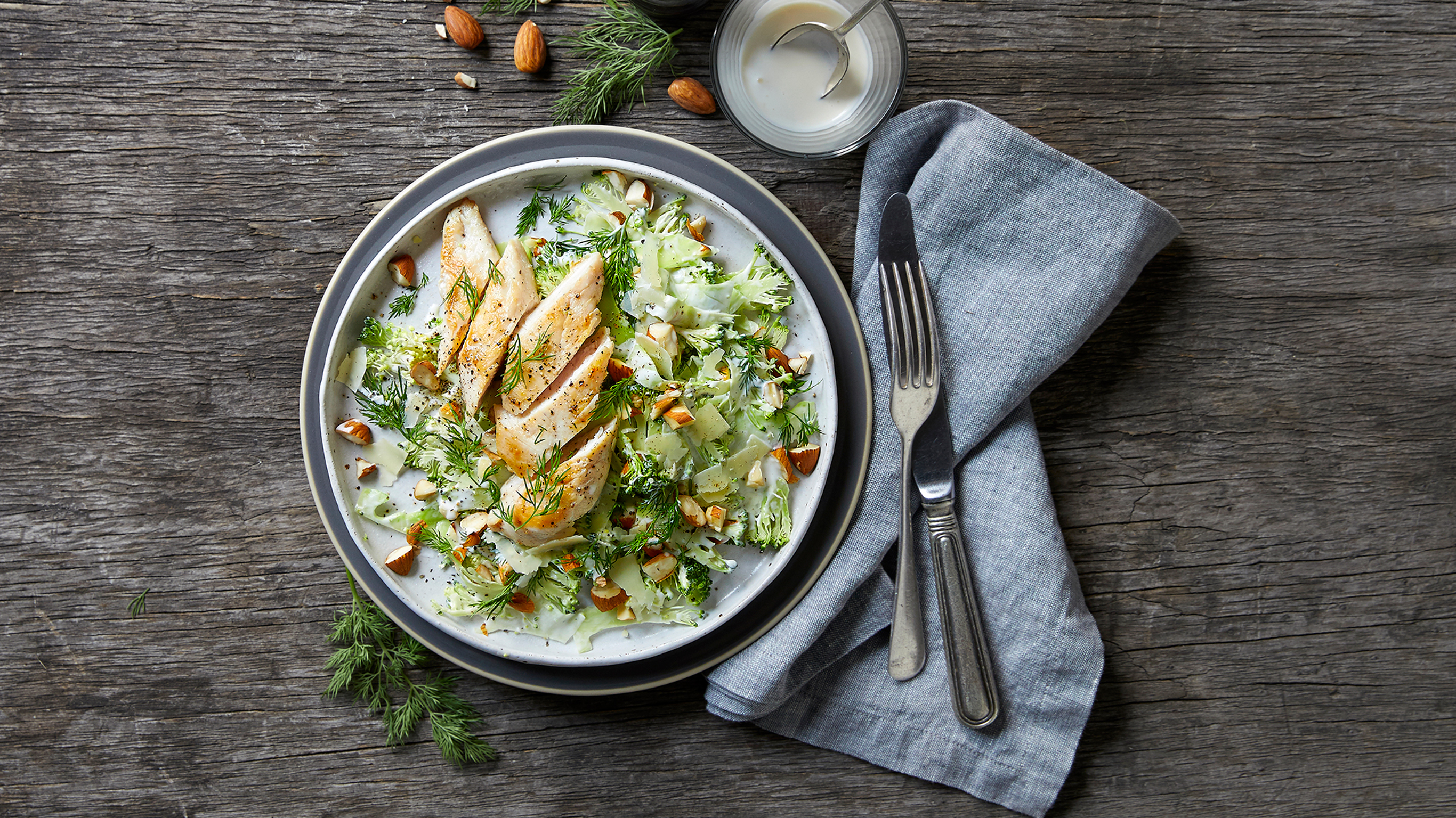 A plate of Centr's Grilled Chicken with Broccoli Salad sits on a wooden table, ready for eating.