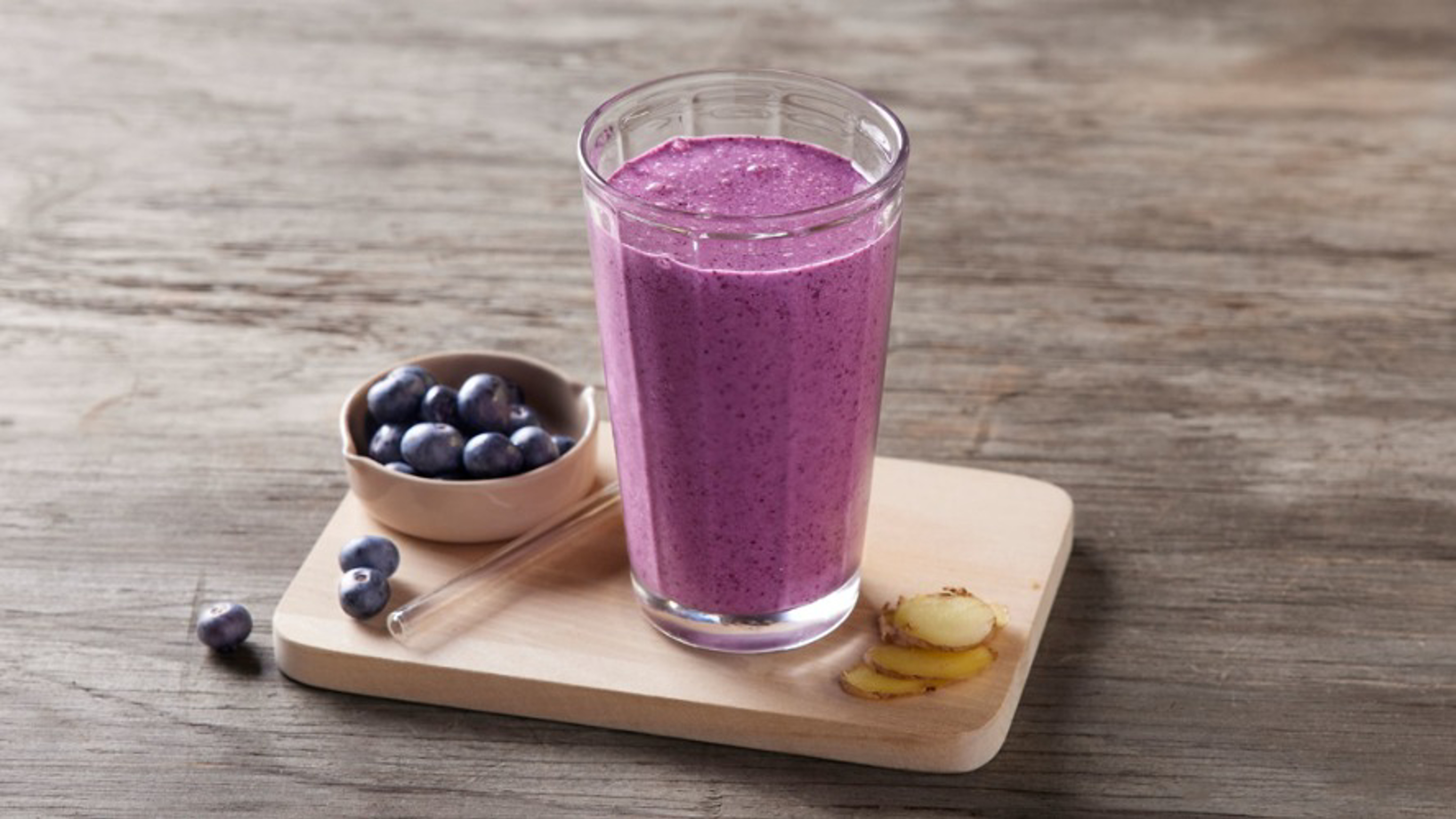 Ange sips a green smoothie from a straw while standing in the kitchen