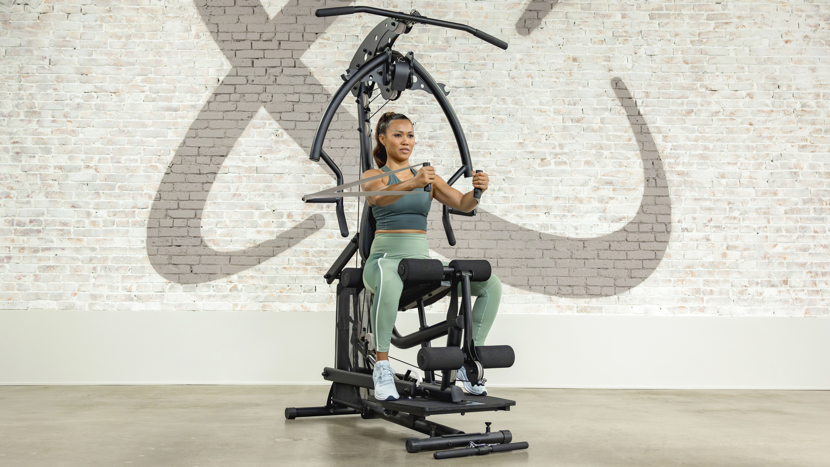 Centr trainer Maricrix Lapaix, wearing coordinated green gym clothes, performs a seated workout on the Centr Bodywieght home gym.