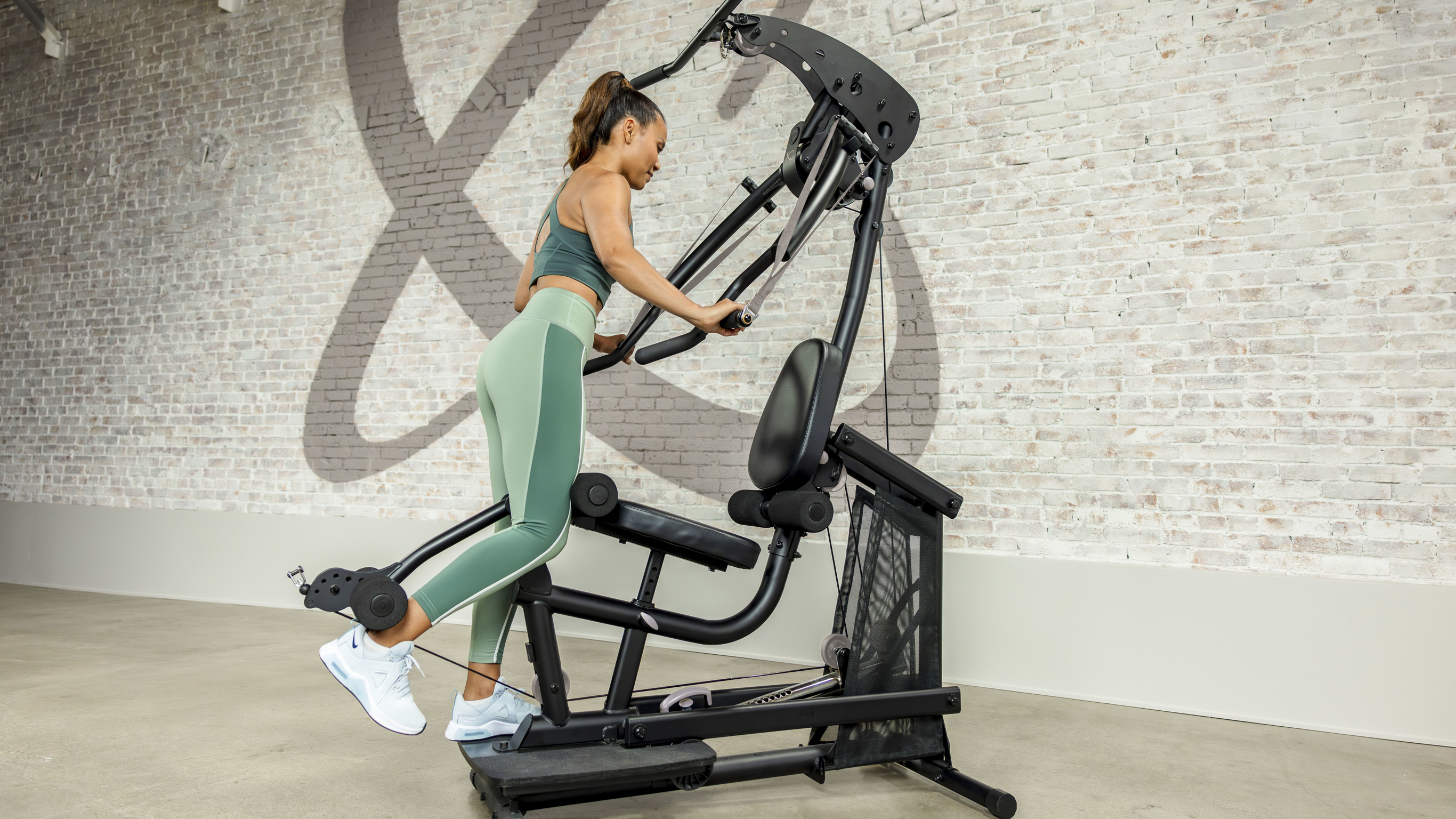 Centr trainer Maricrix Lapaix, wearing coordinated green gym clothes, performs a hamstring exercise on the Centr Bodyweight Home Gym.
