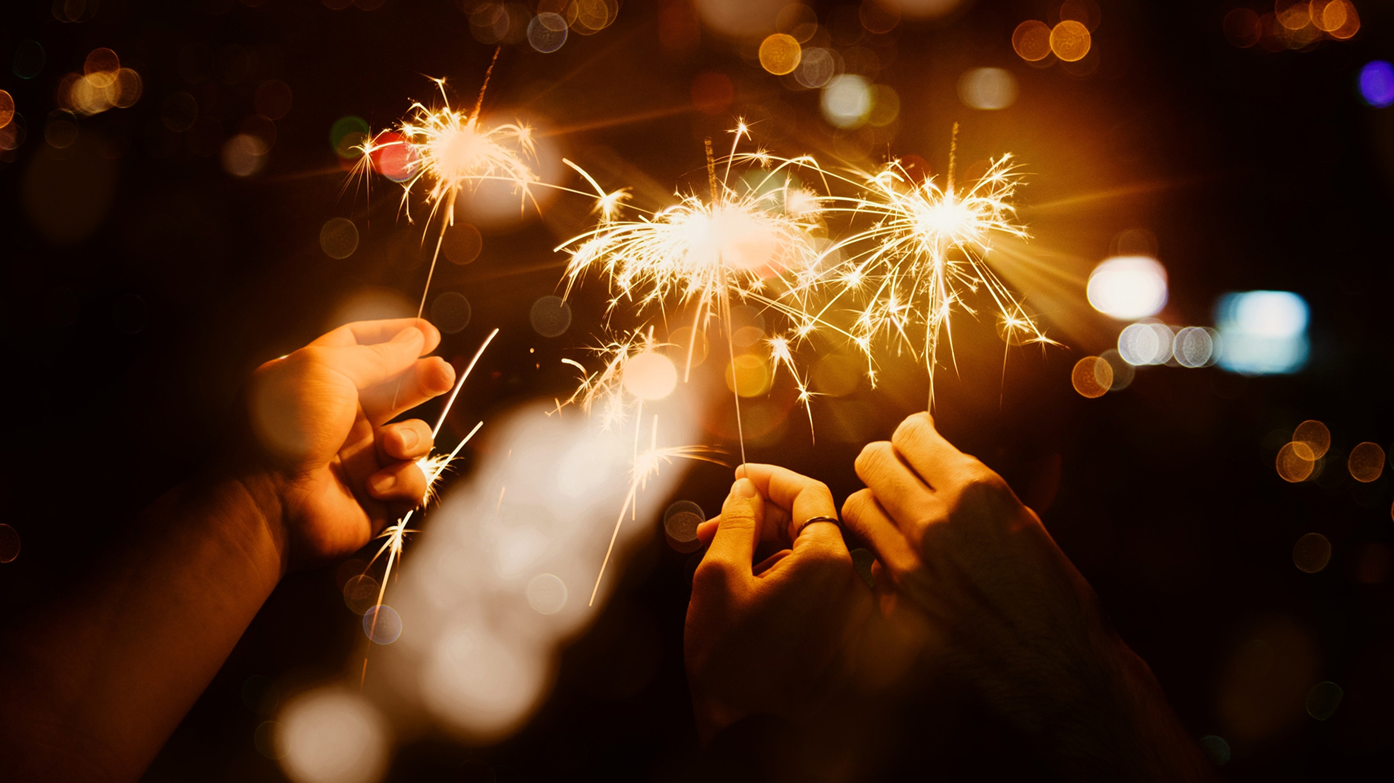 Three hands holding sparklers.