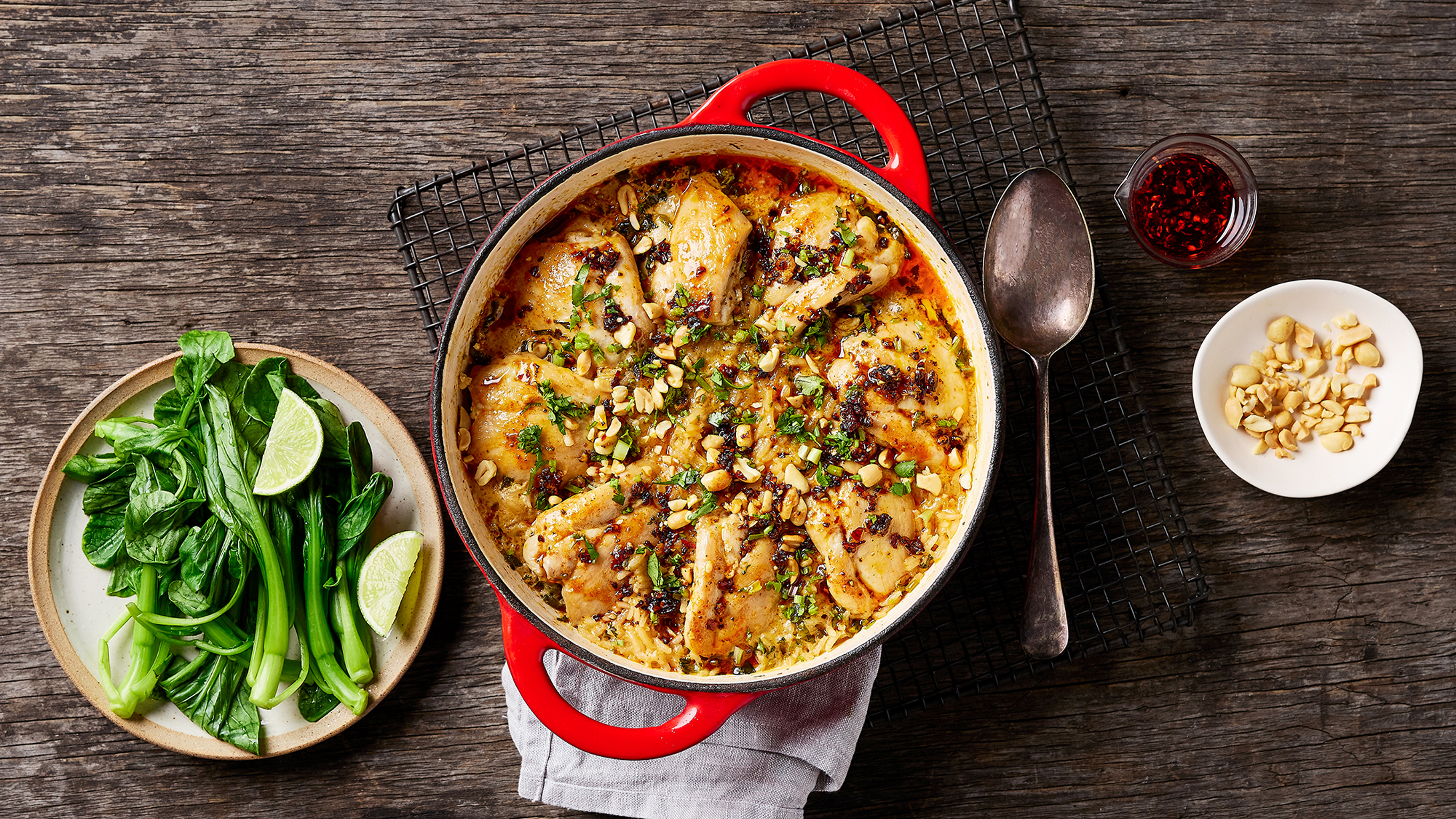 A red enamal baking pot of Centr's One-pot Sticky Coconut Chicken Rice sit on a grey linen napkin, ready for serving.