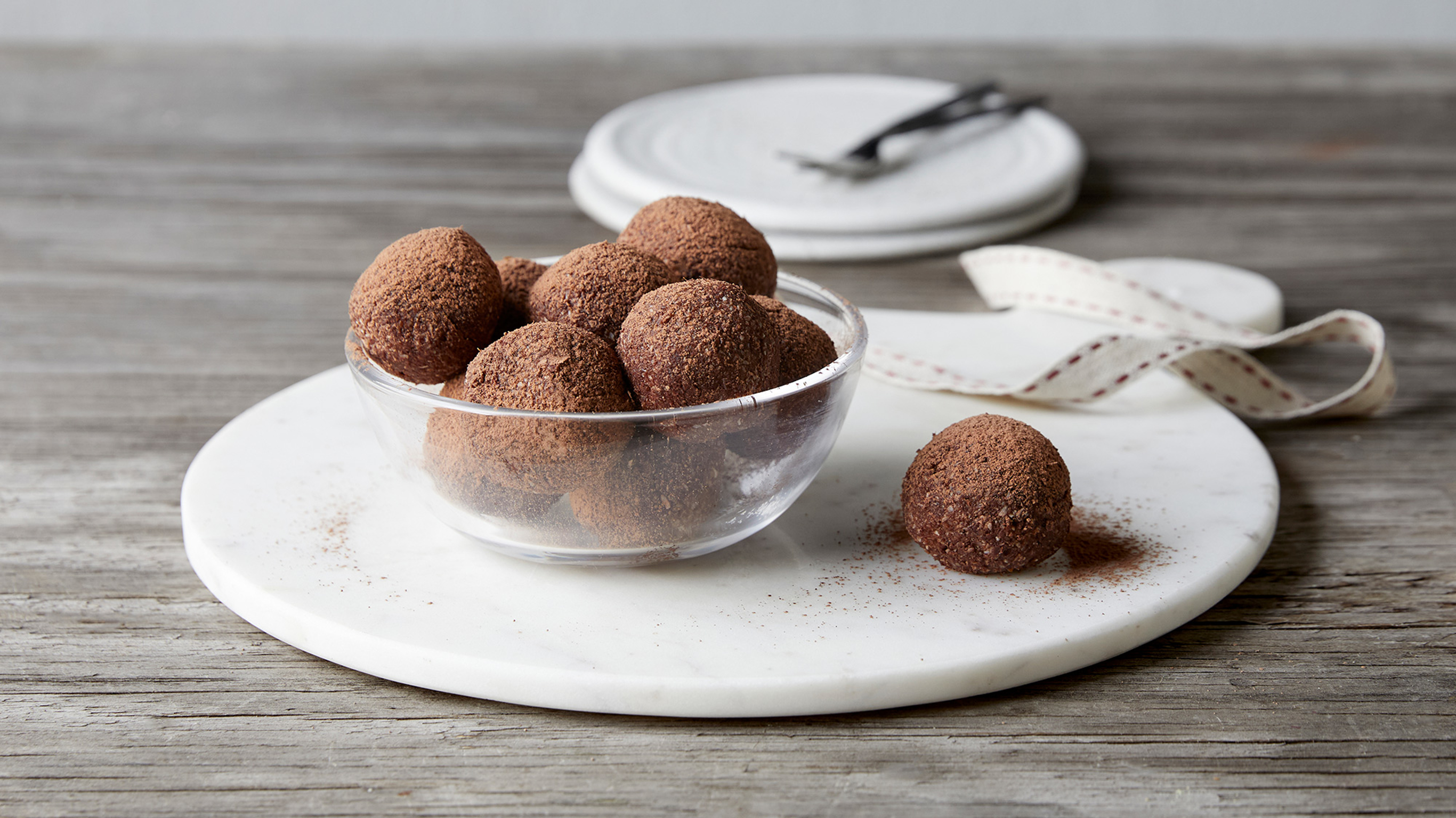 A glass bowl of Centr's Christmas-spiced Chocolate Truffles rests on a plate, with a single truffle on the plate.