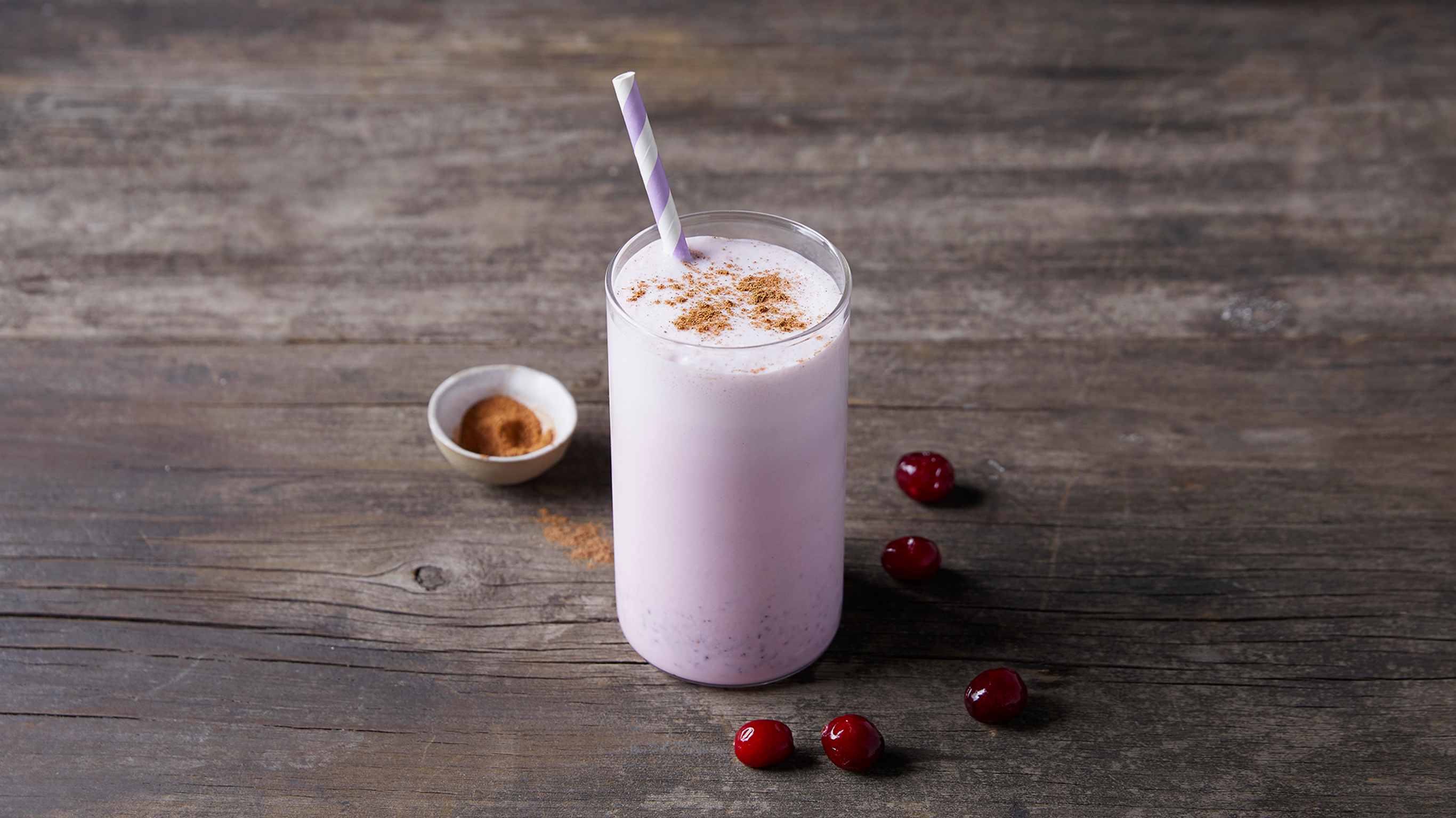 A tall glass of pink Cranberry Spice Smoothie is ready for drinking.