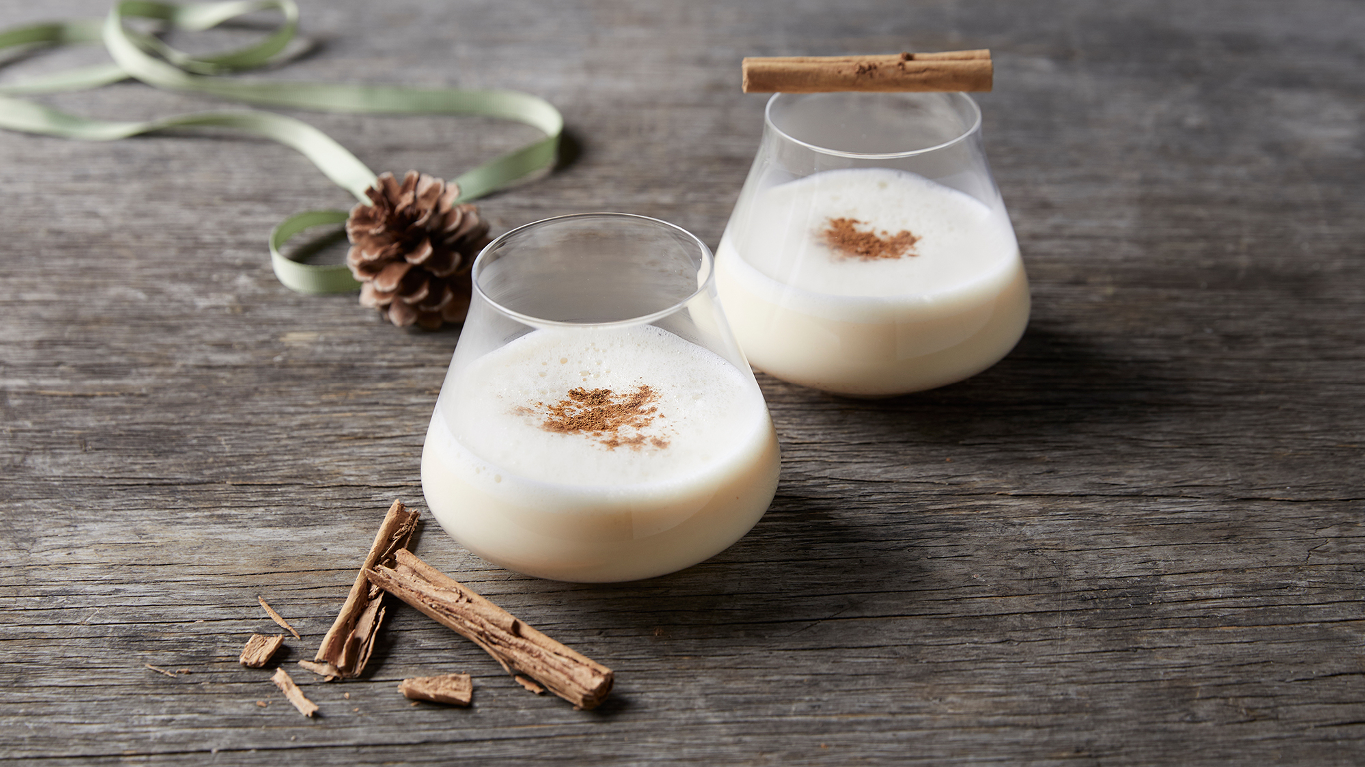 Two tumblers of Centr's Eggnog sit on a rustic table, ready for drinking.