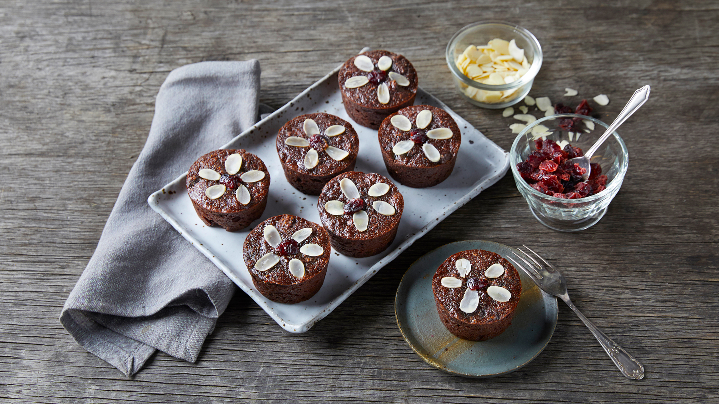 A tray of Centr's Mini Christmas Chocolate Puddings sits on a table, with a single pudding on a plate, ready to eat.
