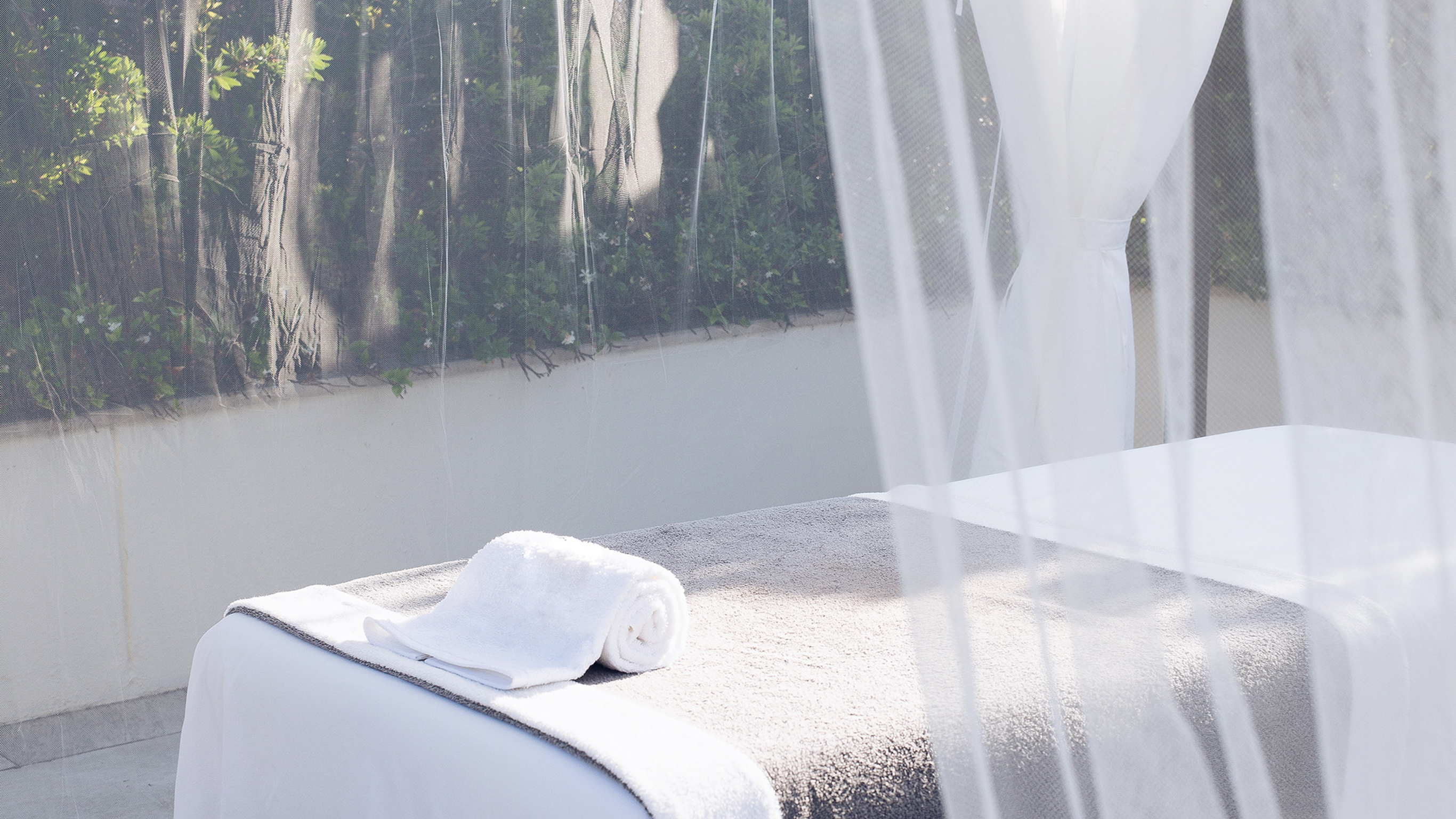A photo of a massage table, behind a thin opaque curtain, with shades of pale grey and white