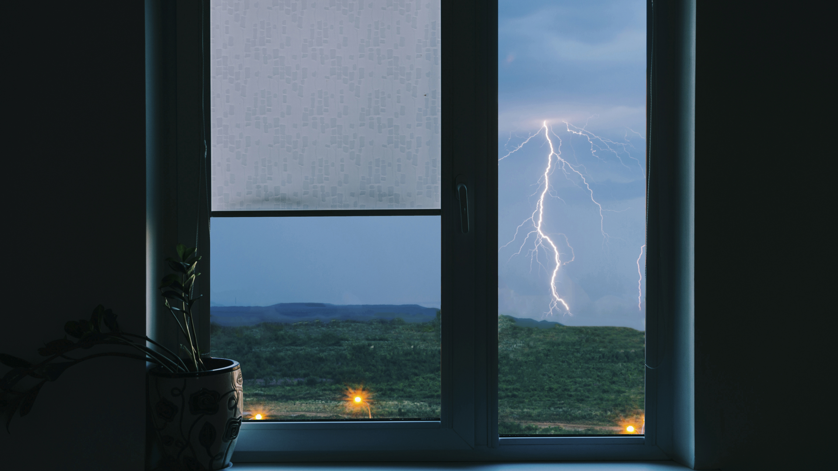 A photo of a line of lightning striking towards the ground, through a wooden window, in the early evening.