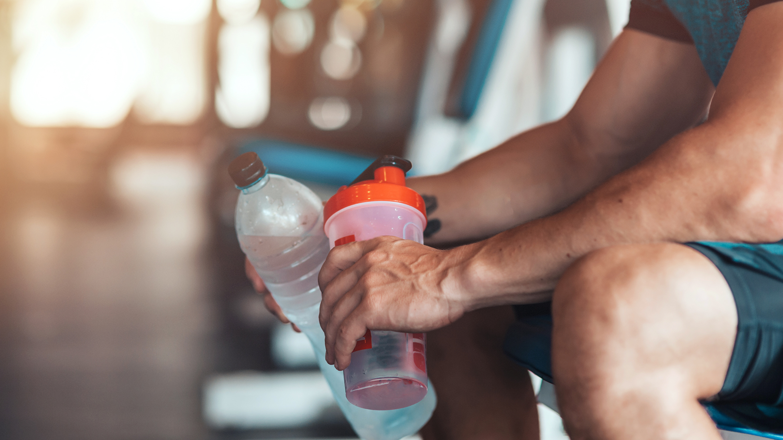 A photo of the hands and knees of a sitting person holding drink bottles in each hand.