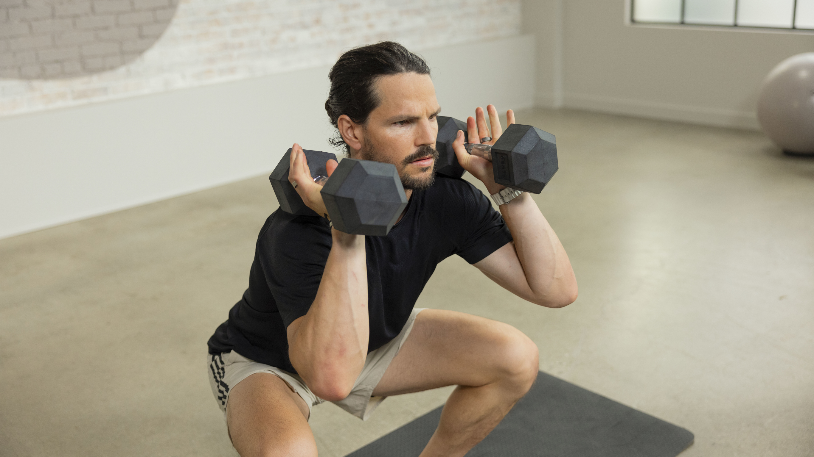 Dan Churchill performs a squat with dunbbells racked on his shoulders.