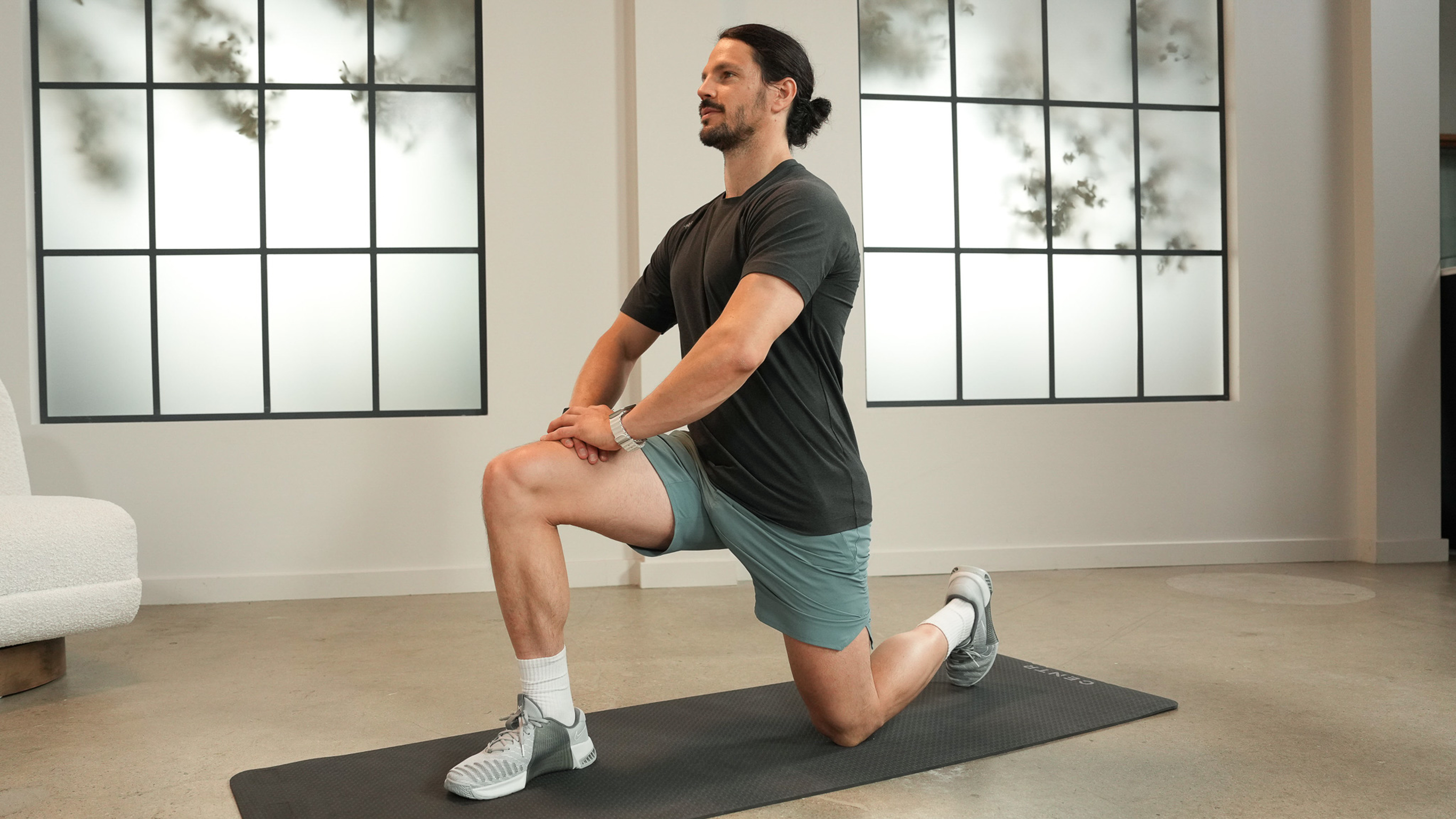 Dan Churchill,  in two-tone grey gym gear, performs a kneeling hip flexor stretch.