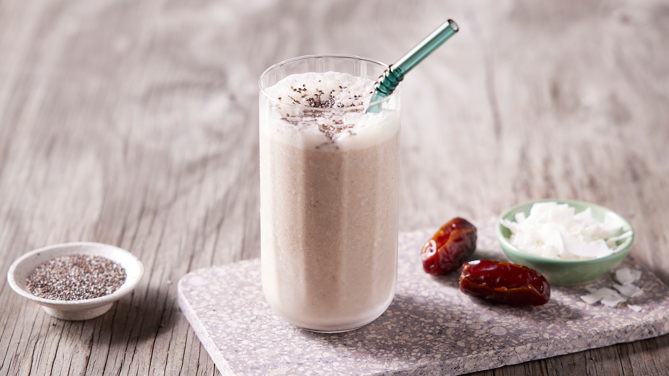 A tall glass of Centr's Coco-caramel Energy Smoothie sits on a square marble board, with a metal straw, ready for drinking.