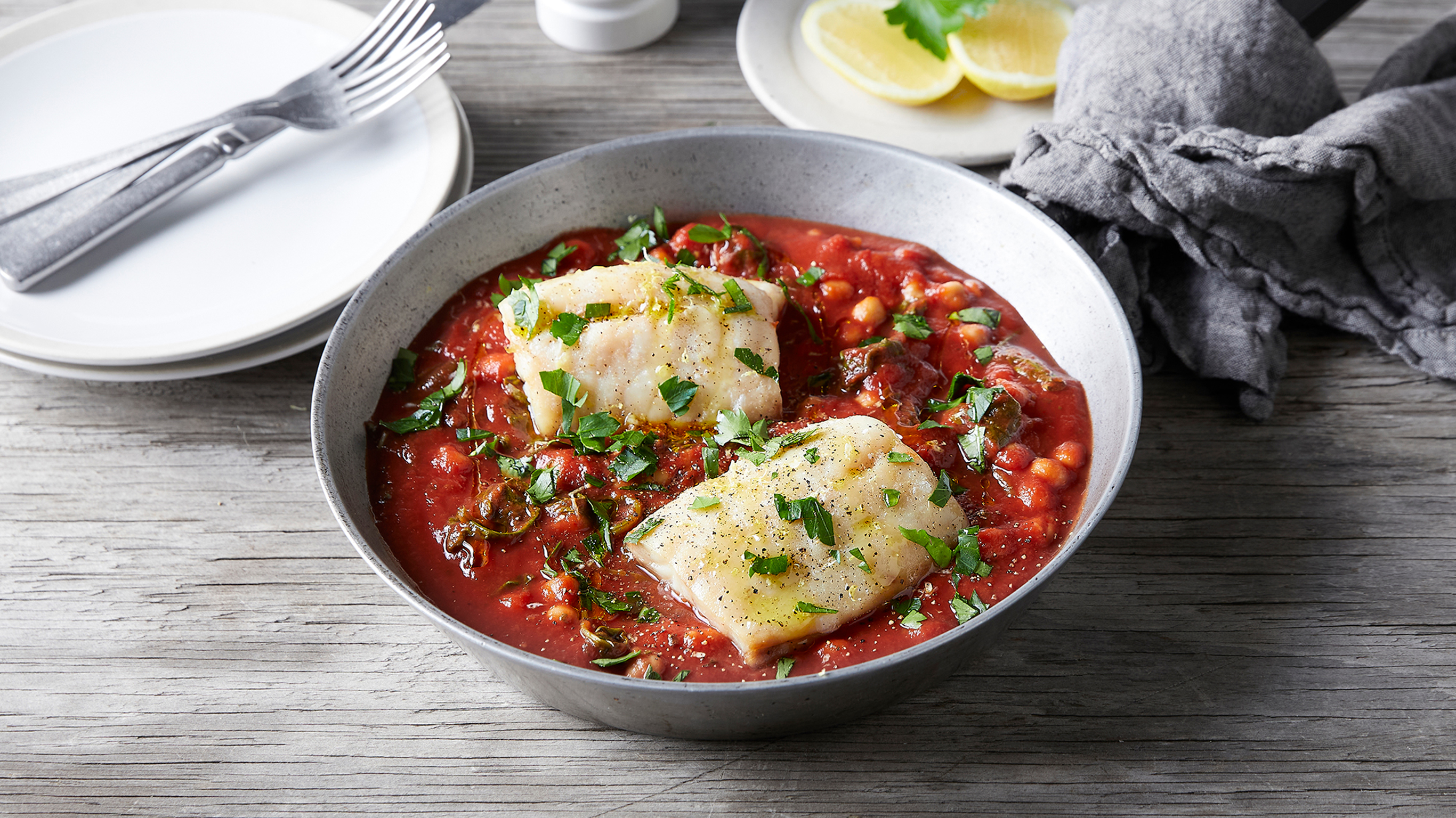A round bowl with a serviing of Centr's Snapper Tray Bake with Spicy Tomato, Chickpeas & Spinach is ready for eating.