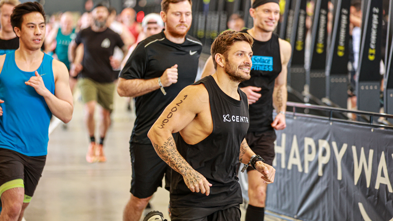 Luke Zocchi, lachend, neemt de bocht in een indoor HYROX-looponderdeel.