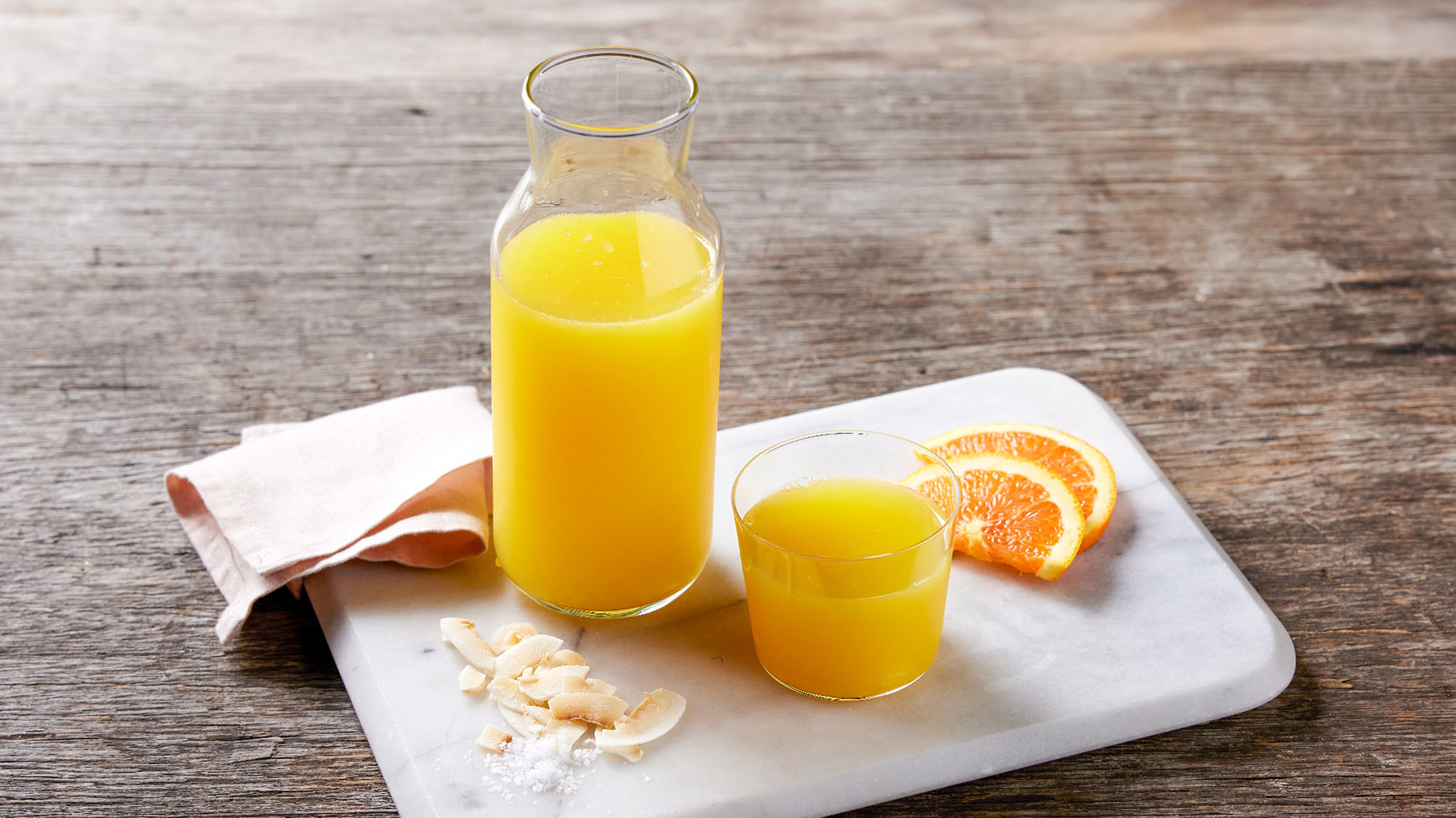 Een hoge glazen fles en een glas met Centr's Citrus Sports Drink naast sinaasappelschijfjes.