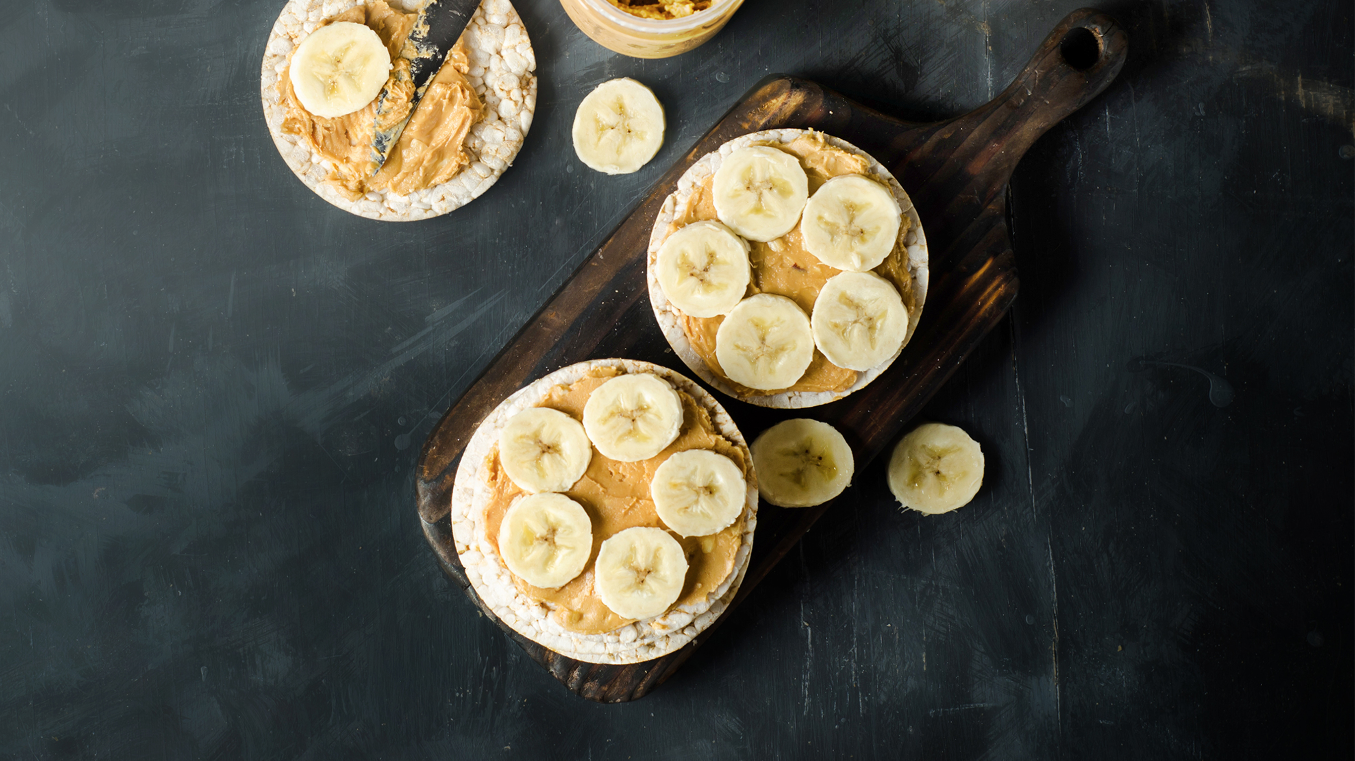 Three rice cakes with peanut butter and sliced bananas are ready for eating.
