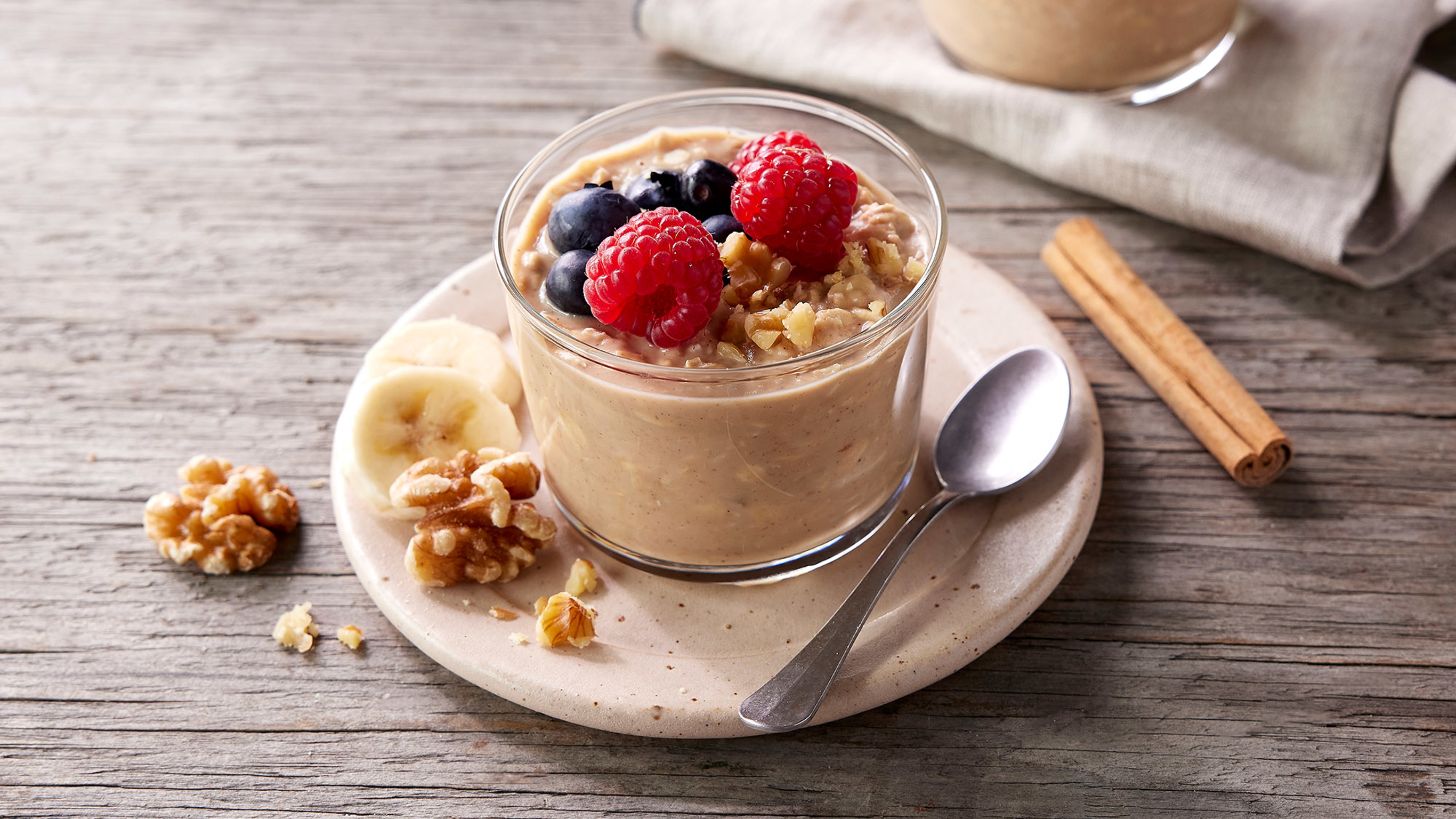 A small glass of Centr's Maple Walnut Overnight Oats sits on a saucer, decorated with fresh berries, ready for eating.