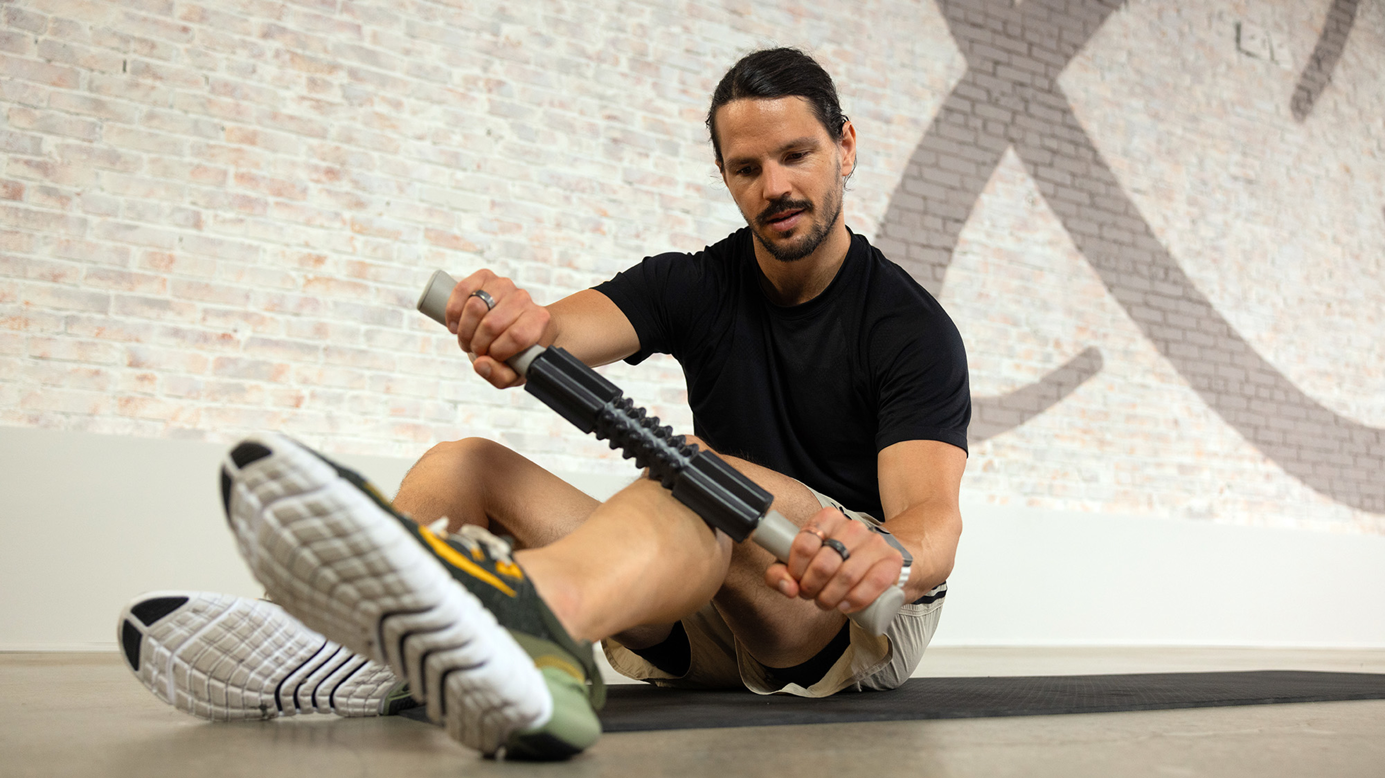 Dan Churchill sits on the floor and uses a Centr roller to massage his lower legs.
