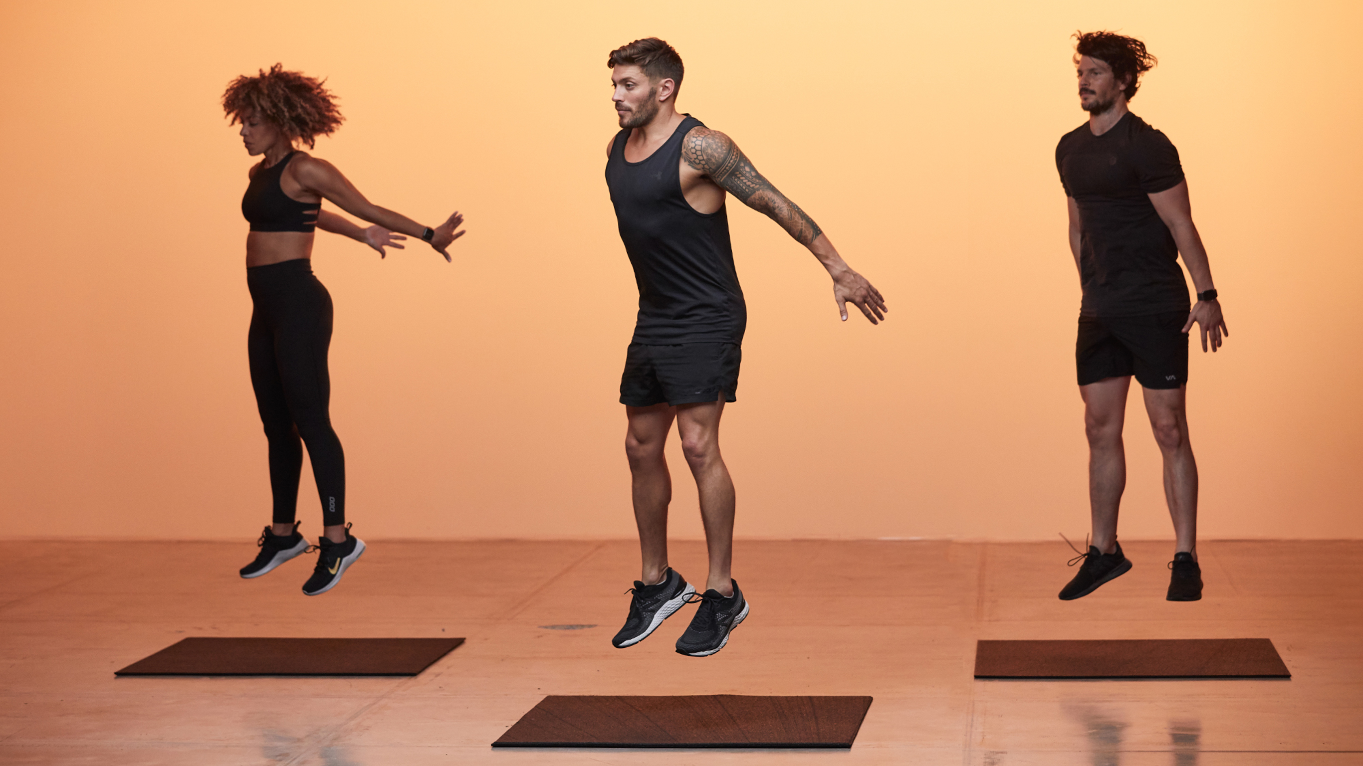 Luke Zocchi, Dan Churchill and Ashlee Joi are all airborne, about to land on their gym mats, doing  a HIIT workout.
