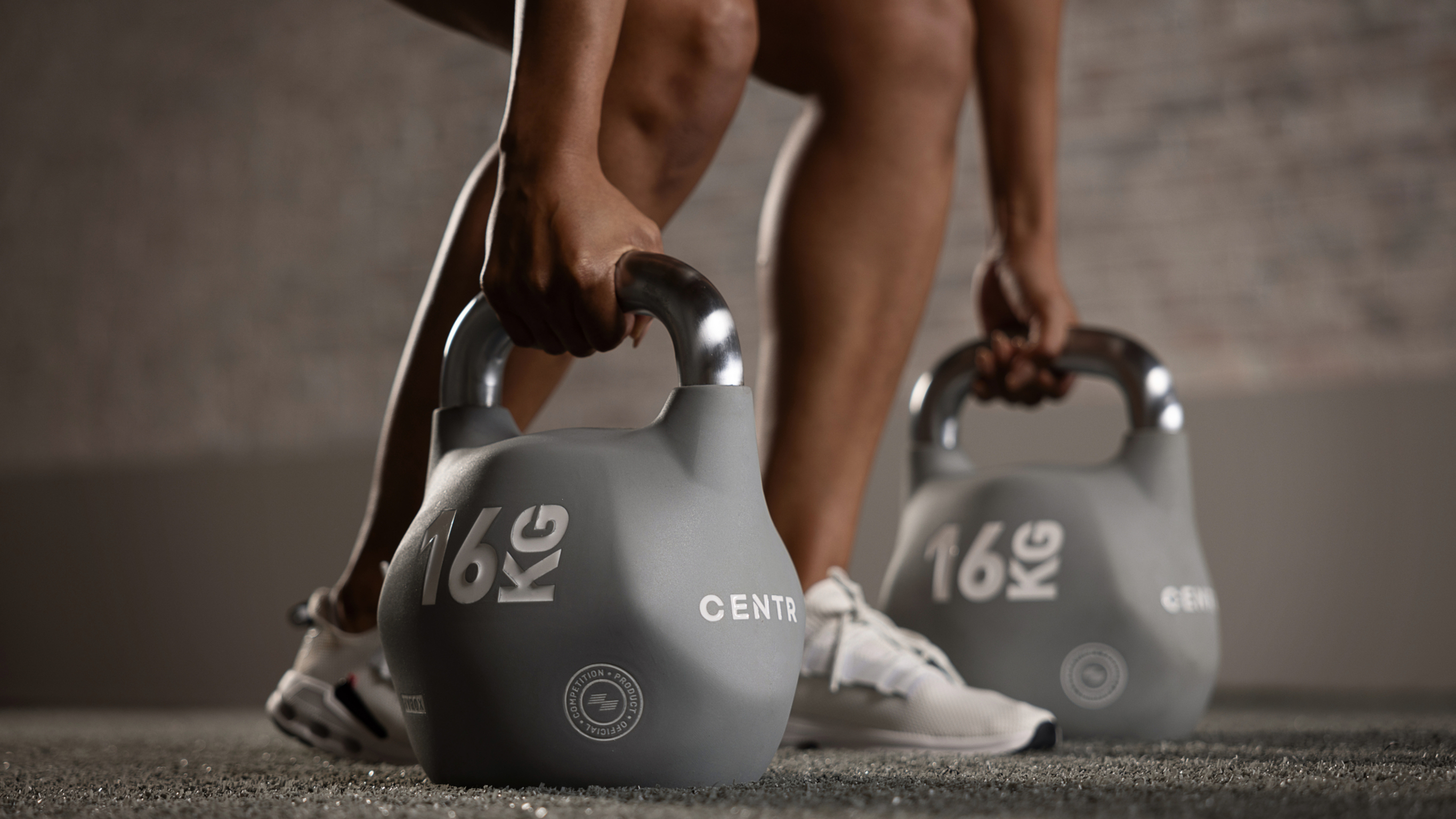 A photo of Maricrix Lapaix's lower legs and feet as she reaches down to grasp a pair of kettlebells on either side of her feet.